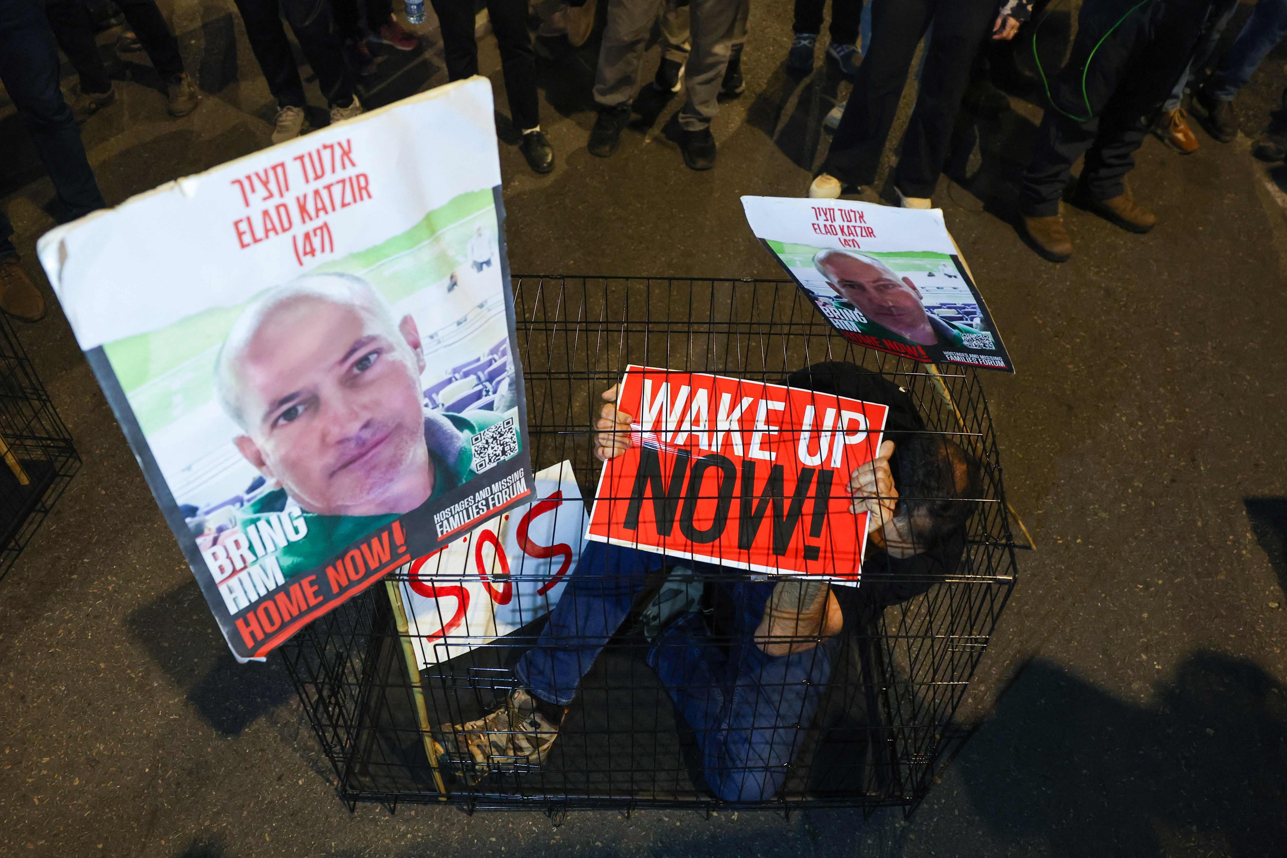 A man sits in a cage with portraits of 47-year-old Israeli hostage Elad Katzir as relatives and supporters of Israeli hostages held in Gaza stage a demonstration in Tel Aviv. Photo: AFP
