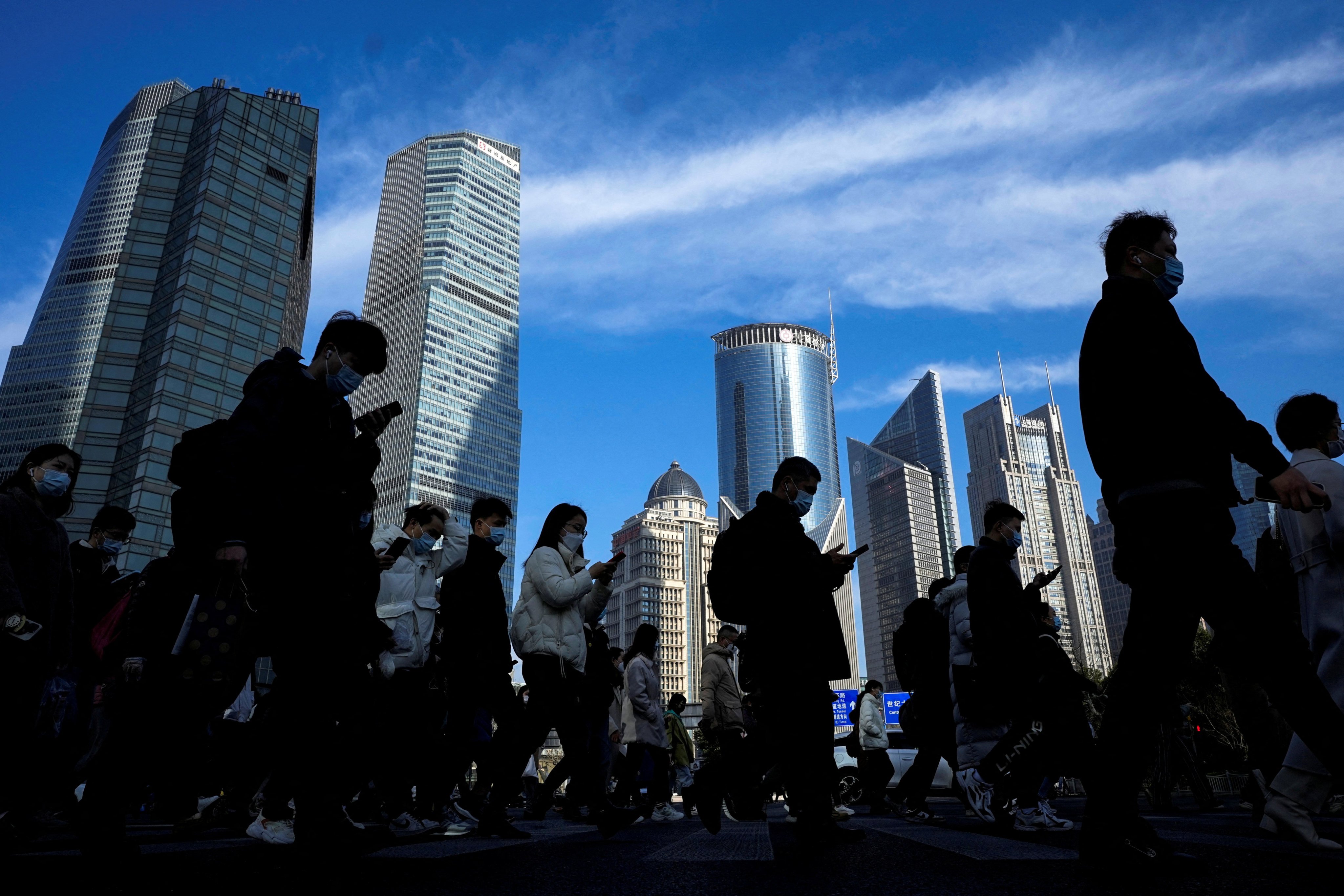 People cross a street near office towers in the Lujiazui financial district of Shanghai on February 28, 2023. Photo: Reuters
