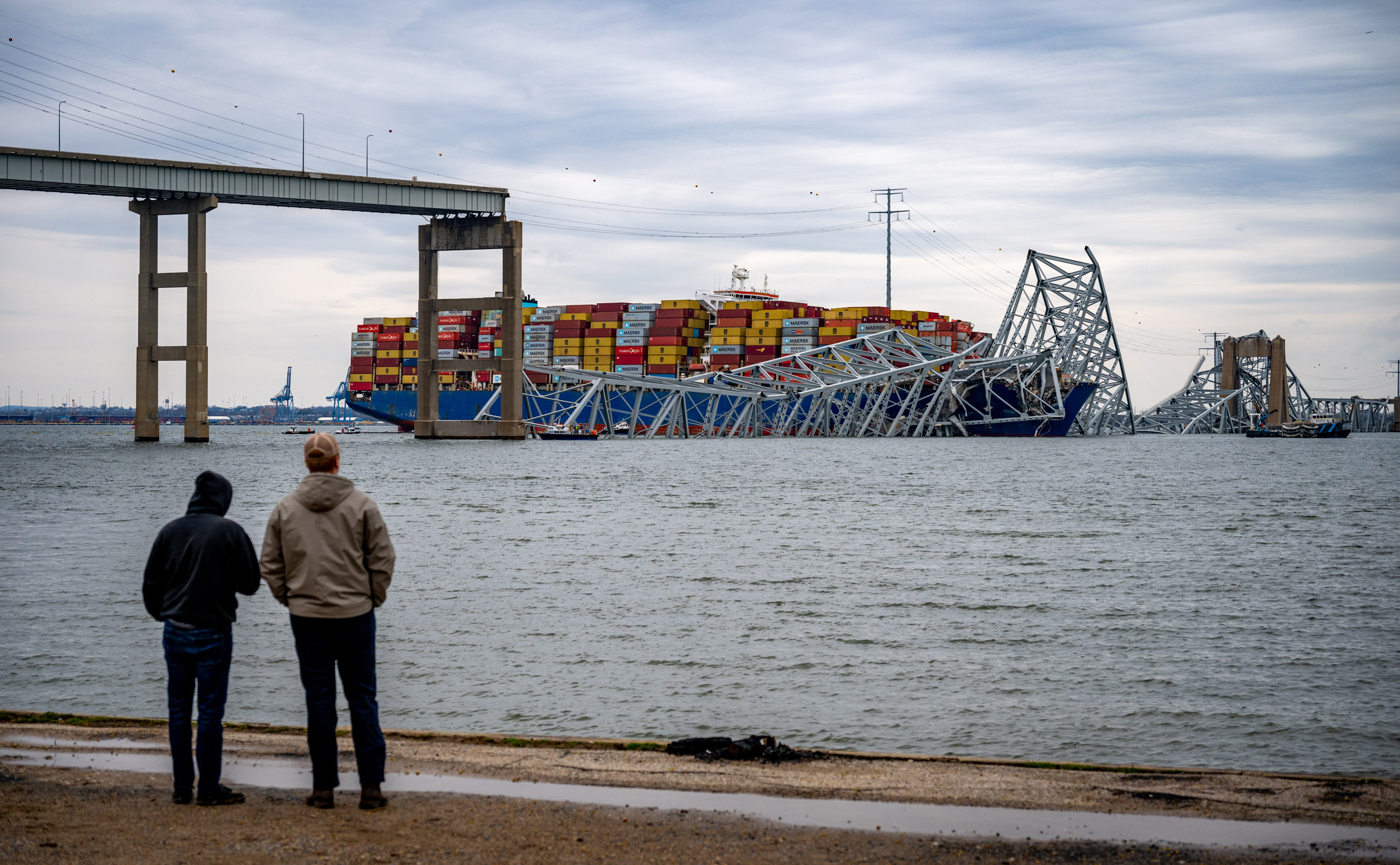 Two men at Fort Armistead Park look at the twisted structure and road decking from the Francis Scott Key Bridge draped across the bow of the container ship Dali. Photo: TNS