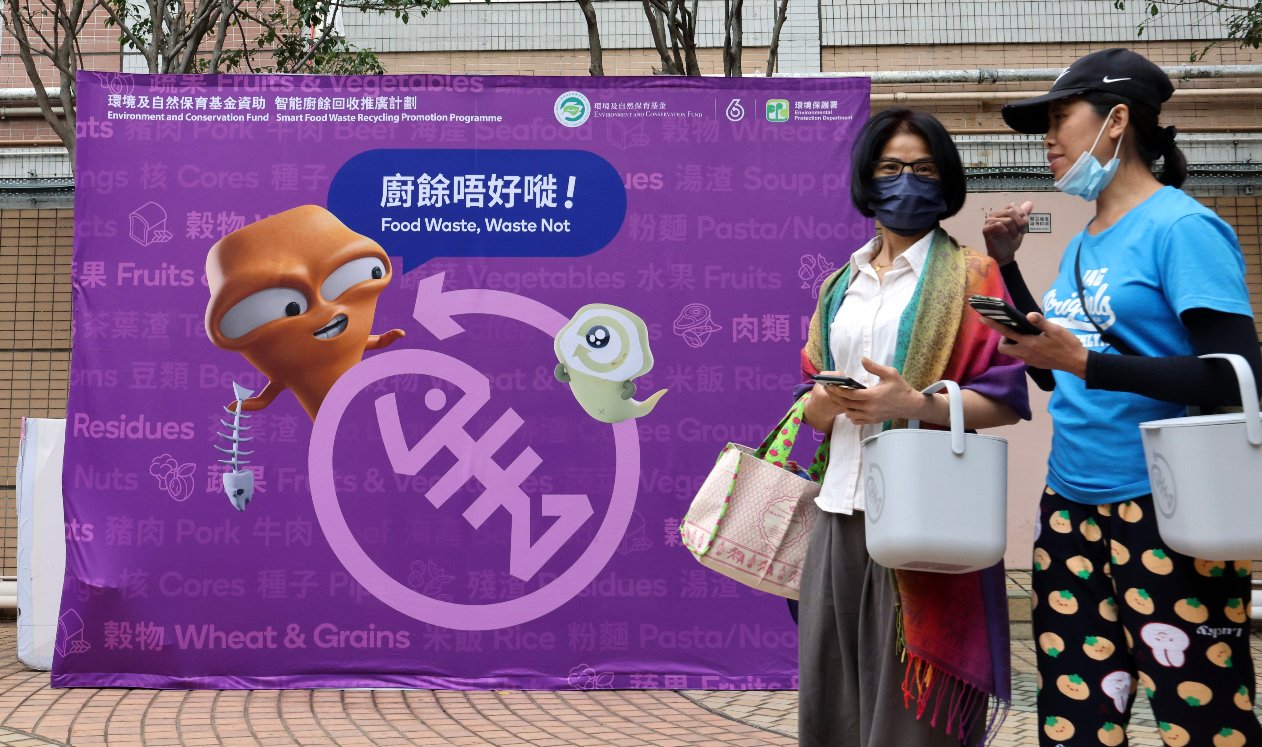 Residents carrying food waste disposal canisters walk past a poster promoting less wastage at Moon Lok Dai Ha in Tsuen Wan on April 9. Photo: Jelly Tse