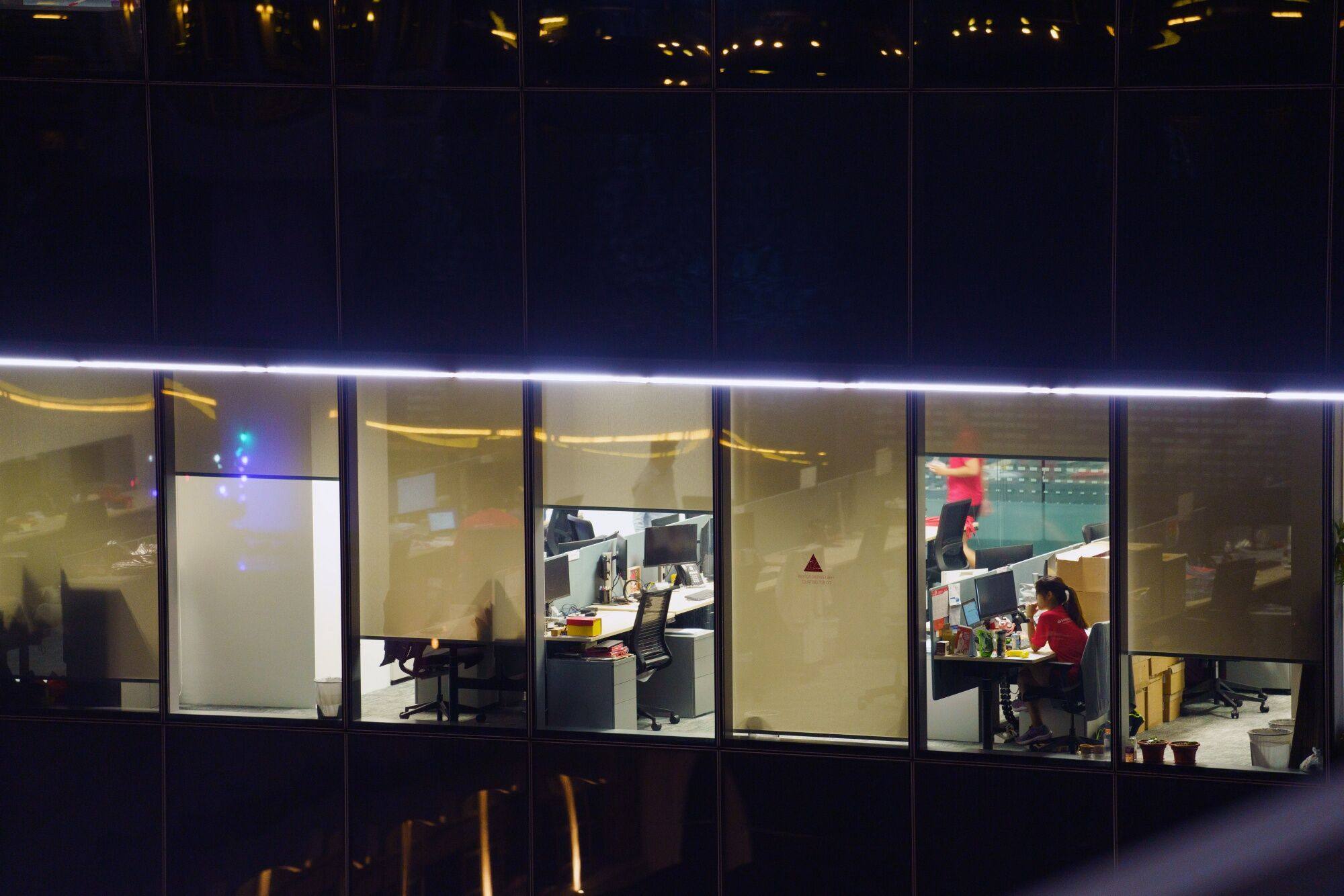 Office workers are seen at night through the windows of a commercial building in the central business district of Singapore. Photo: Bloomberg