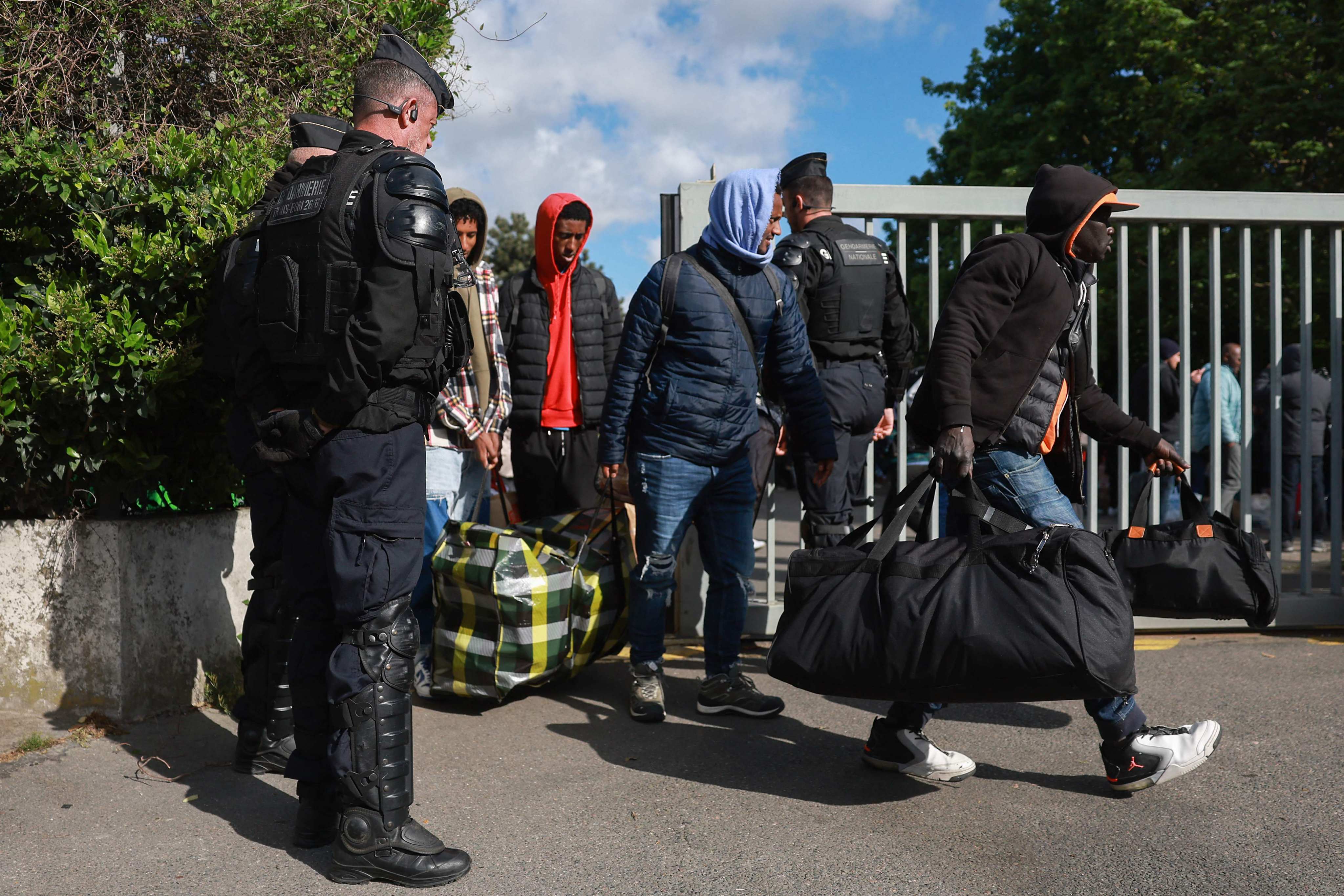 French gendarmes stand guard next to migrants leaving for another location, during the evacuation of France’s biggest squat. Photo: AFP