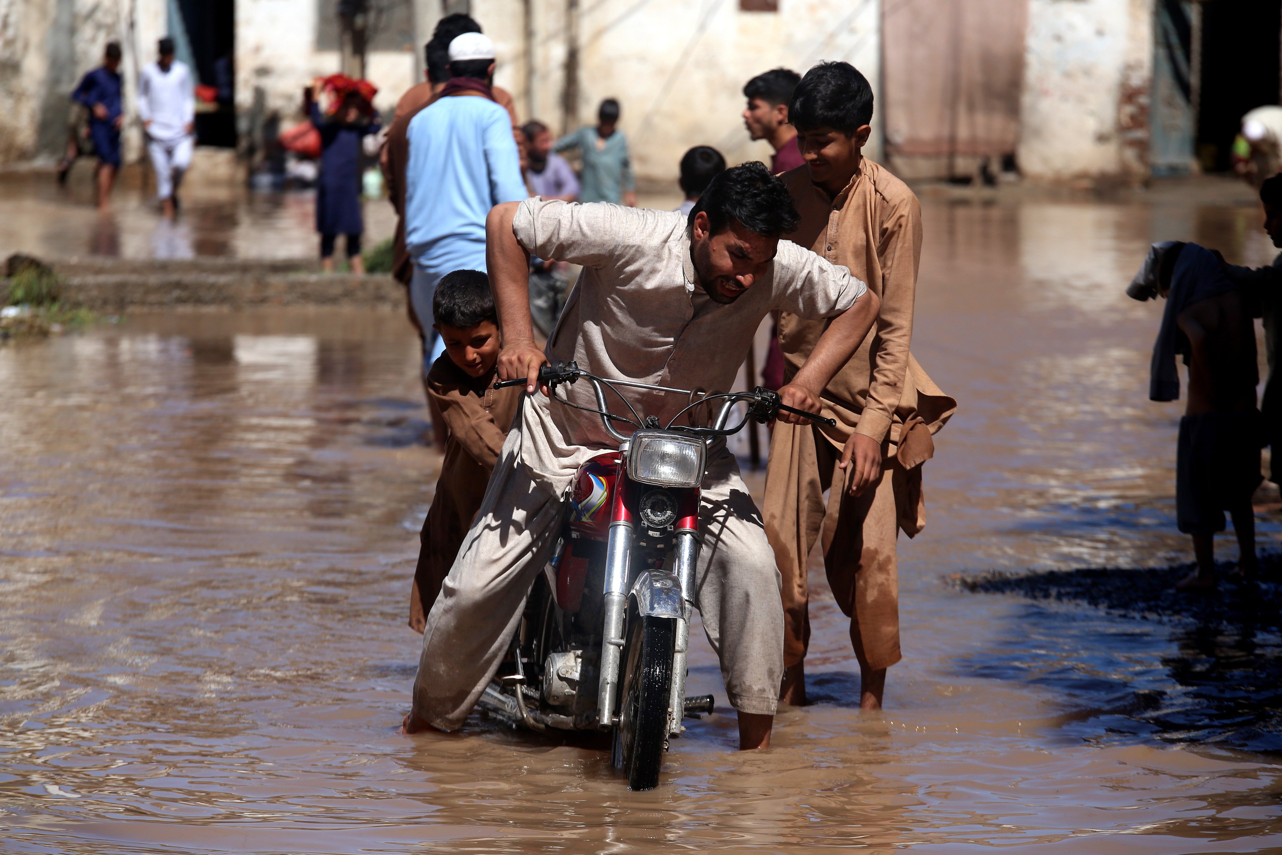 epa11282073 A group of people pushes a motorbike through a flooded street after heavy rain in Khyber Pakhtunkhwa province, Pakistan. Photo: EPA-EFE