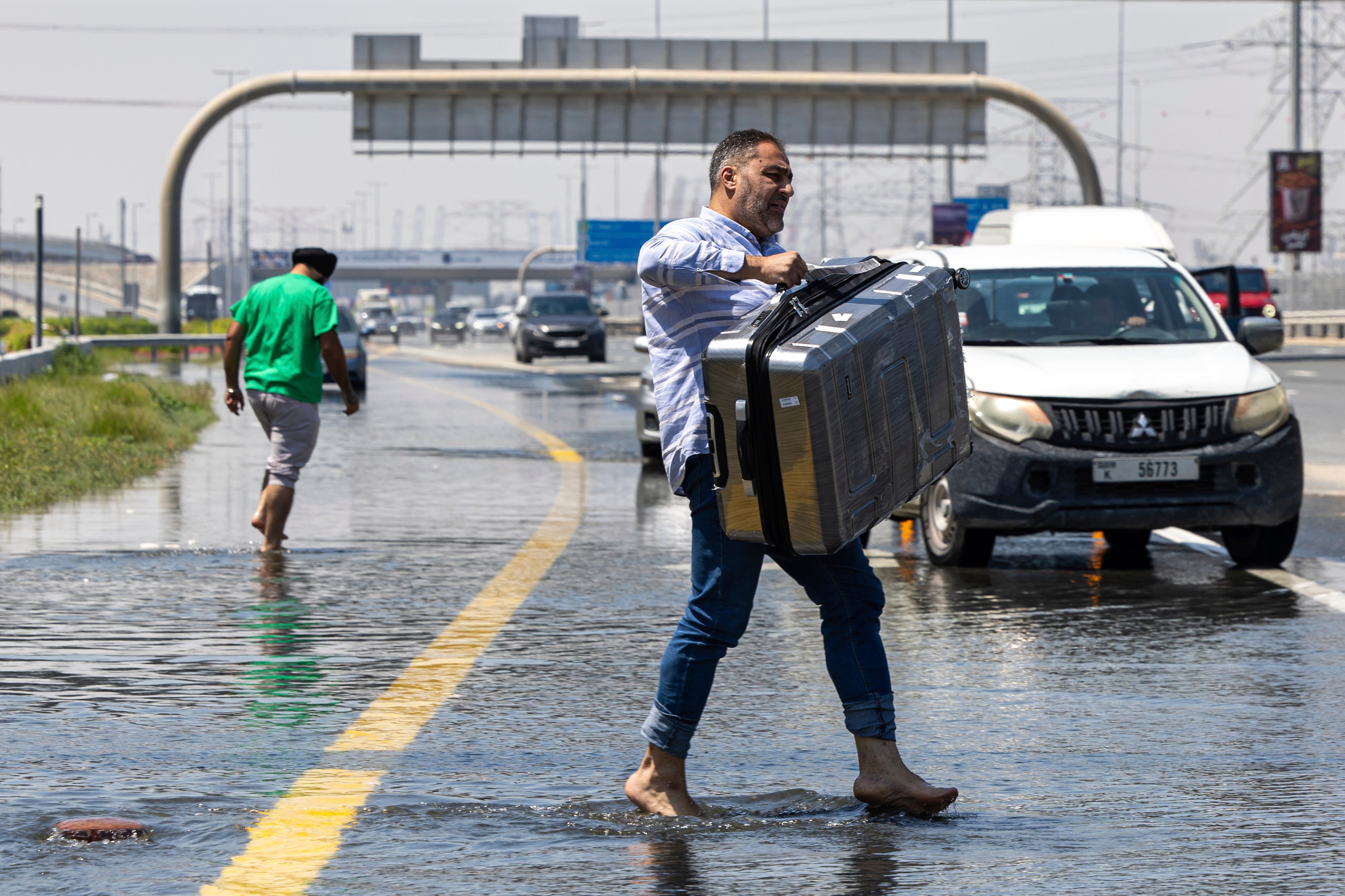A man carries luggage through floodwater on Sheikh Zayed Road highway in Dubai. Photo: AP