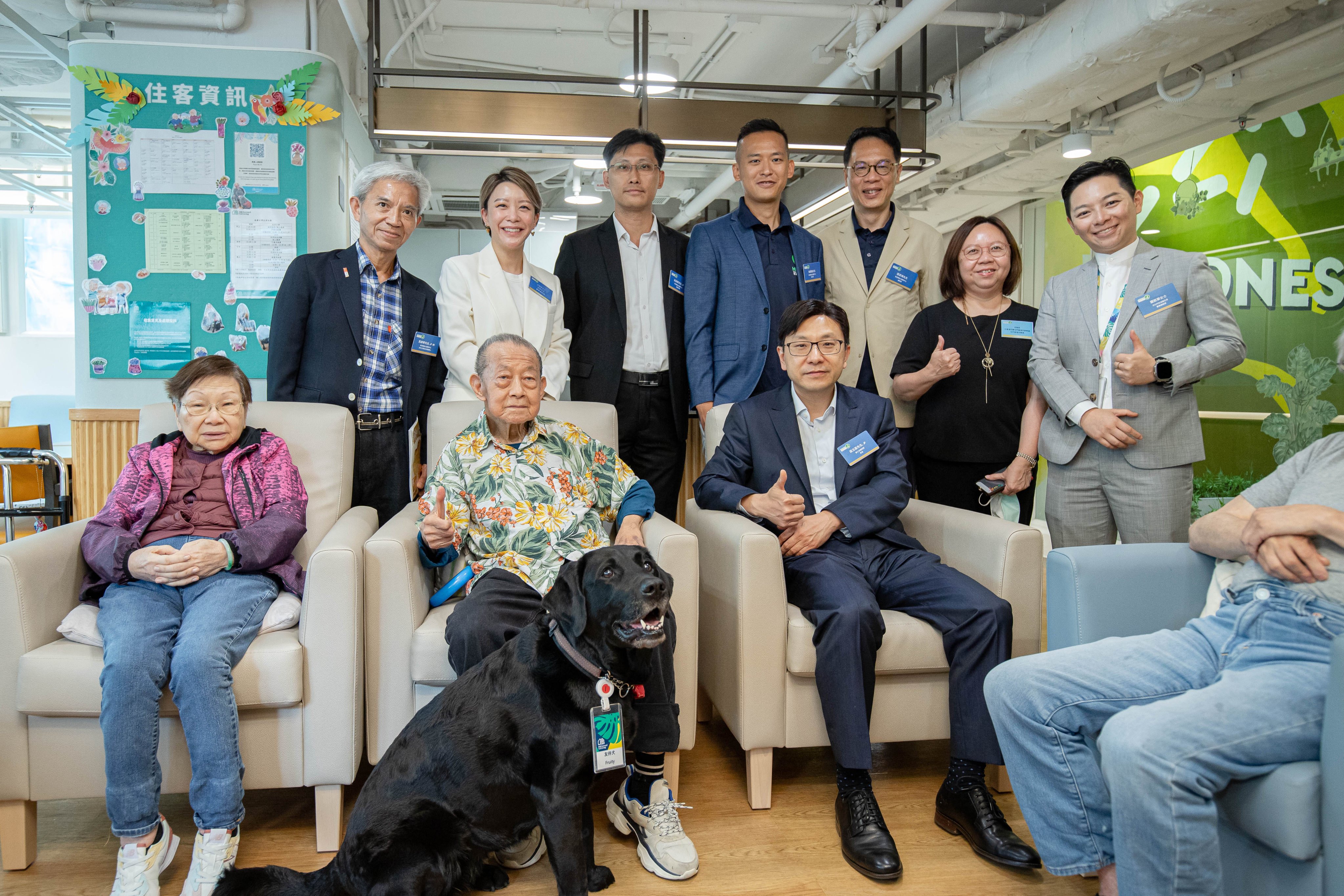 Fruity the dog at the elderly facility in Tuen Mun where she lives, along with (second from lower left) Johnson Ho, resident of the home; (third from lower left) Secretary for Labour and Welfare Chris Sun, and (third from upper right) David Cheung, CEO of HKSEDS. Photo: Handout
