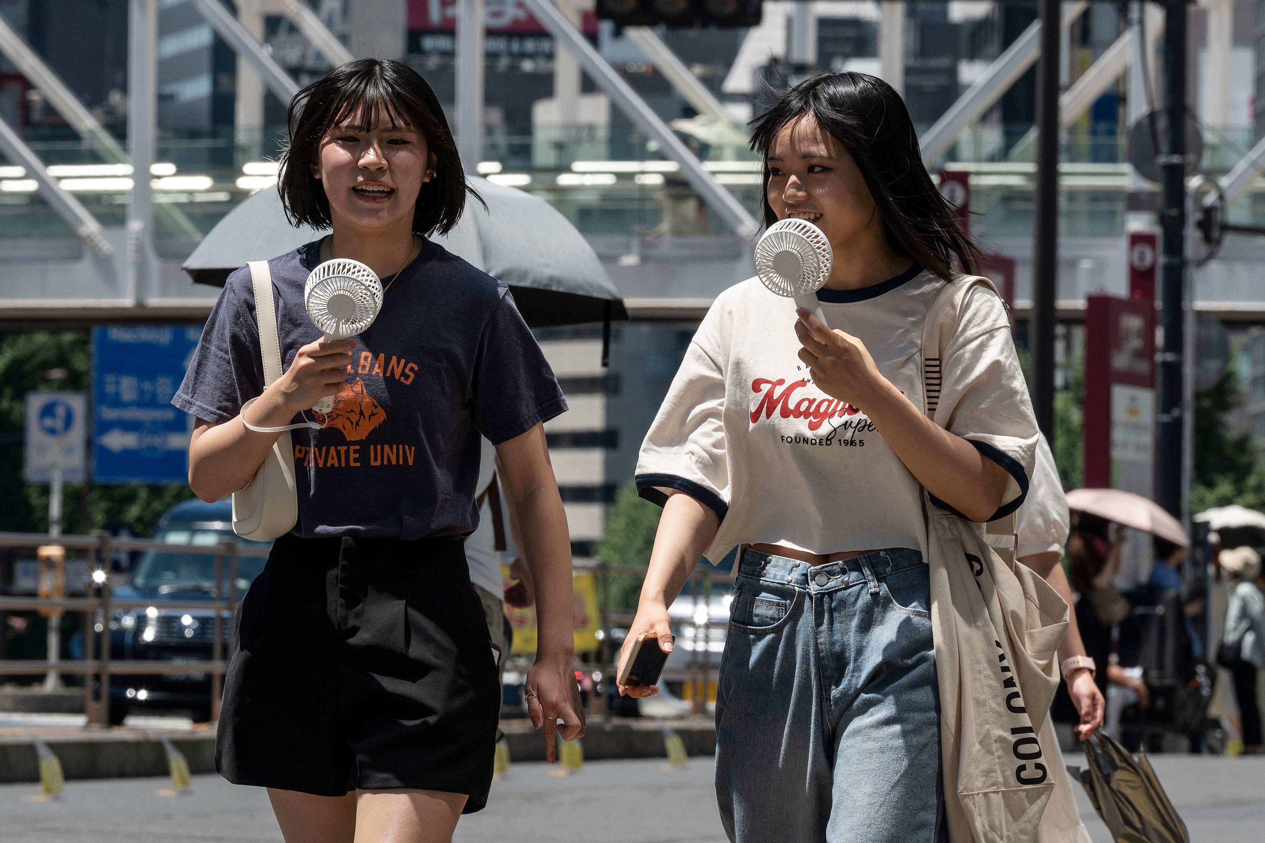 Women use portable fans to cool off while walking around Tokyo last summer. Photo: AFP