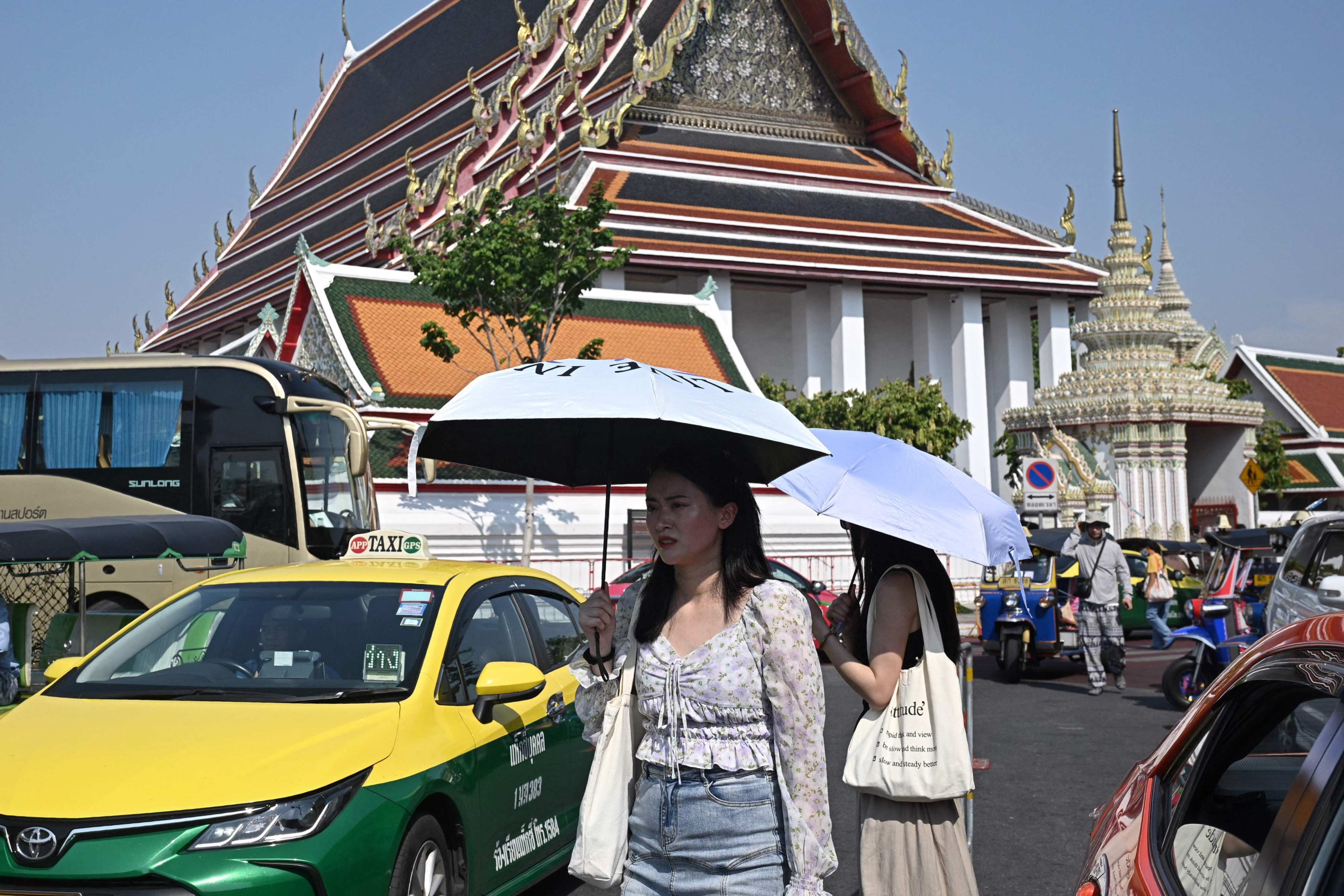 Tourists shield themselves from the sun with umbrellas outside Wat Pho Buddhist temple in Bangkok, Thailand. Photo: AFP