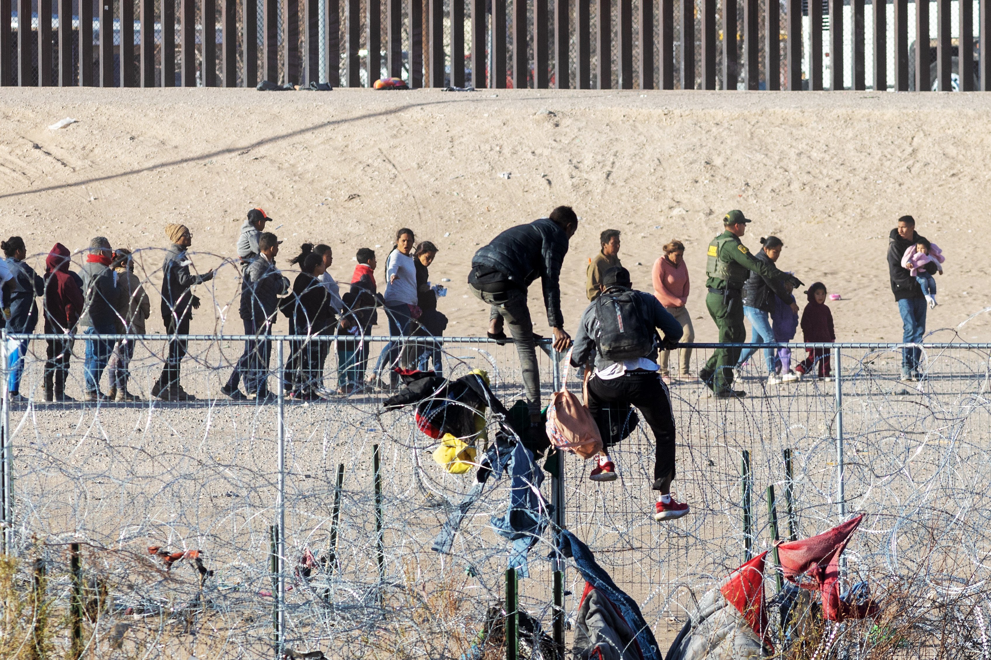 Two men scale fence, as hundreds of migrants queue along the border wall dividing Mexico and the United States, awaiting processing by the US Border Patrol. Photo: dpa