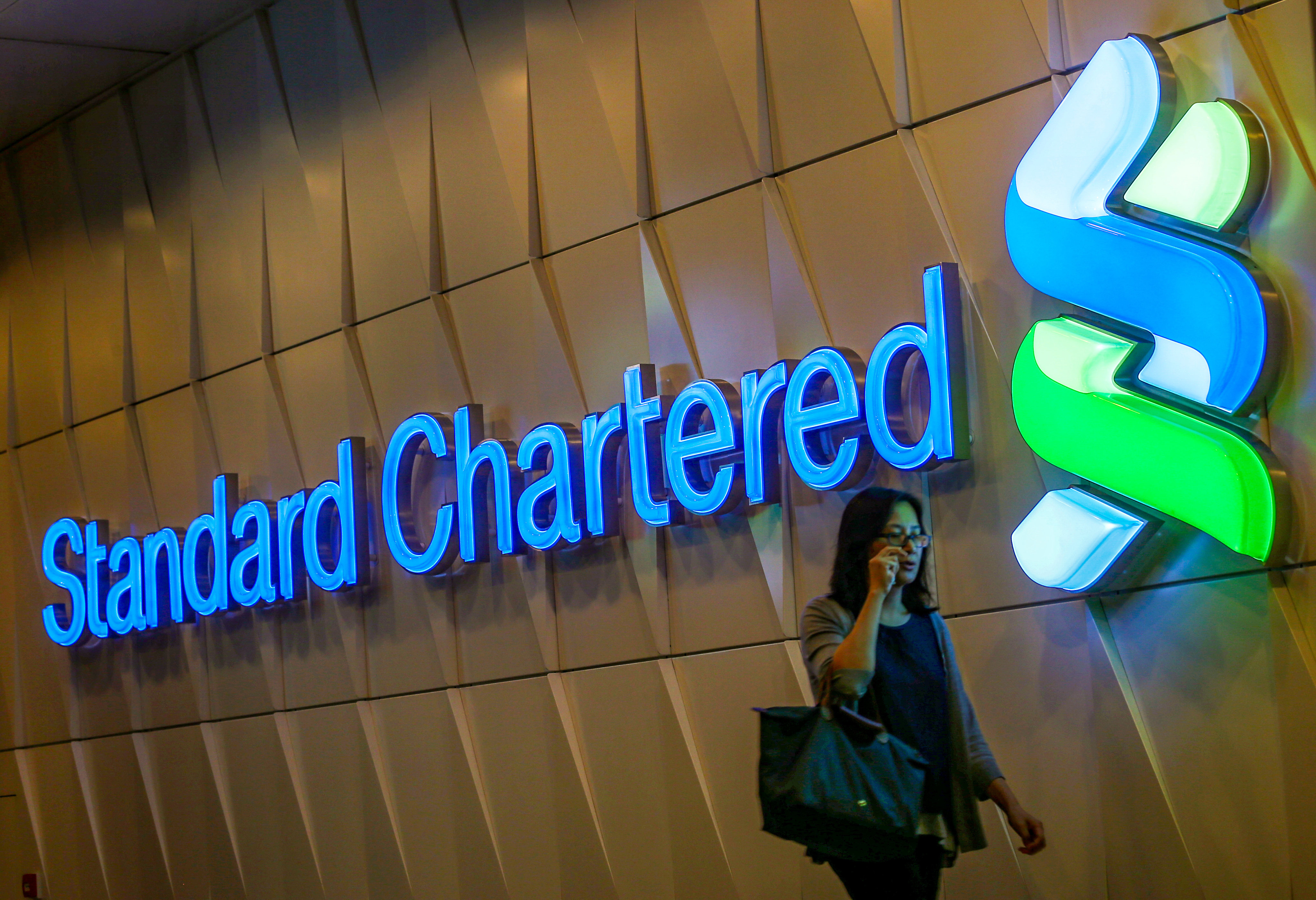 A woman passes a Standard Chartered Bank logo in Central. Photo: K. Y. Cheng