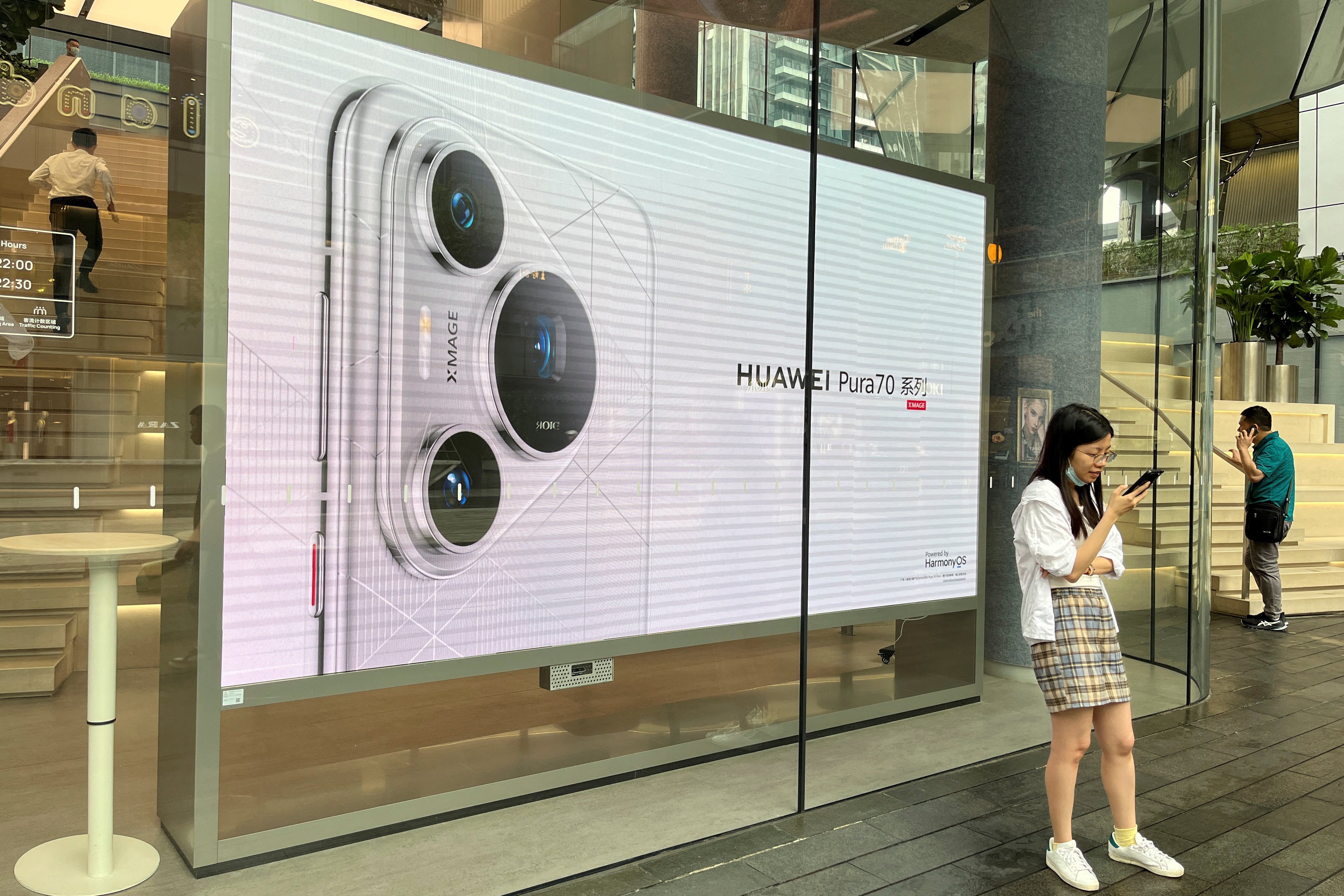 A woman uses her phone in front of an ad for the Huawei Pura 70 series smartphones, outside the company’s flagship store in Shenzhen, China April 26, 2024. Photo: Reuters