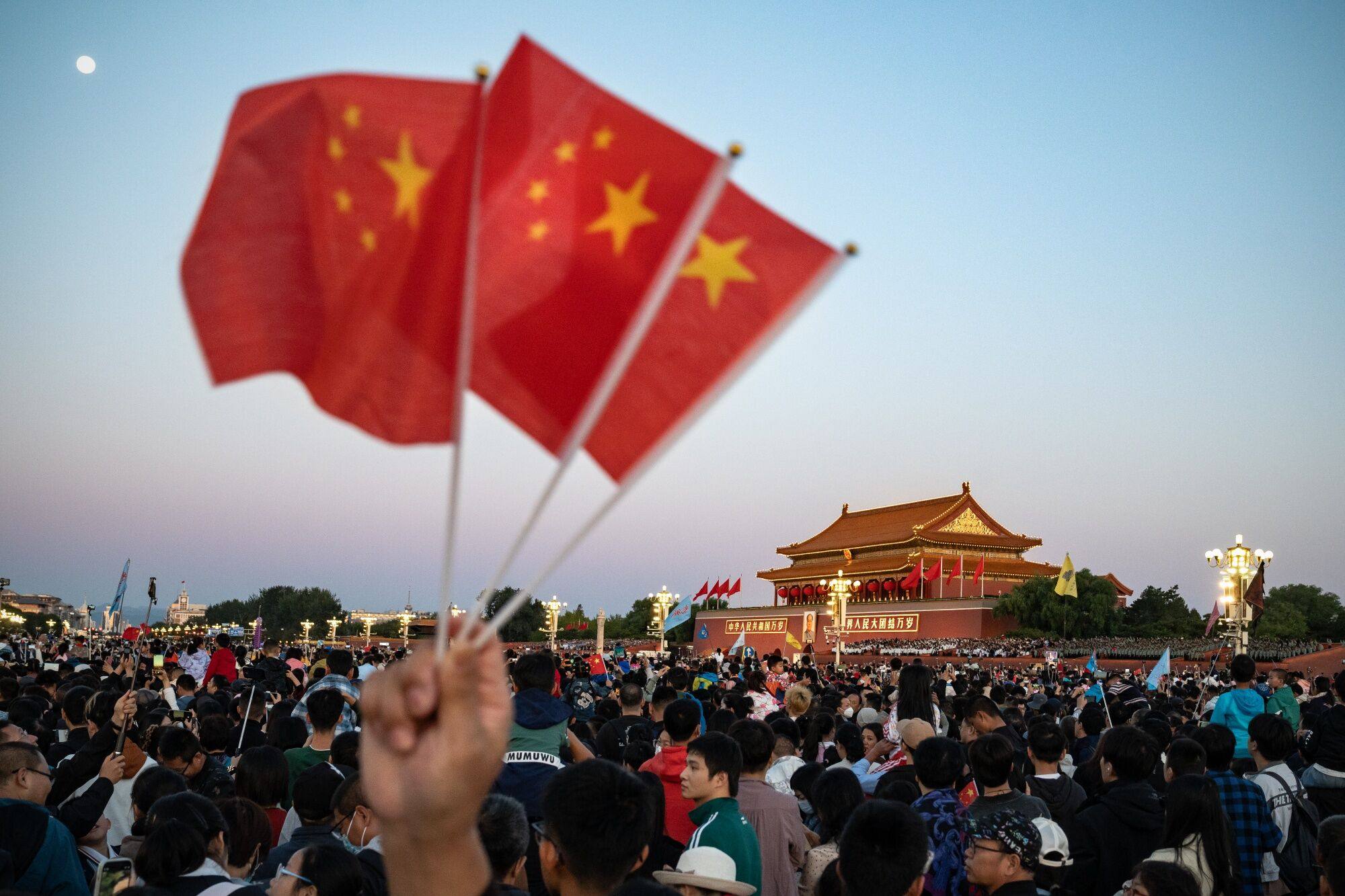 A visitor holds up three Chinese flags as people gather for the flag-raising ceremony at Tiananmen Square to mark National Day in Beijing on October 1, 2023. Photo: Bloomberg