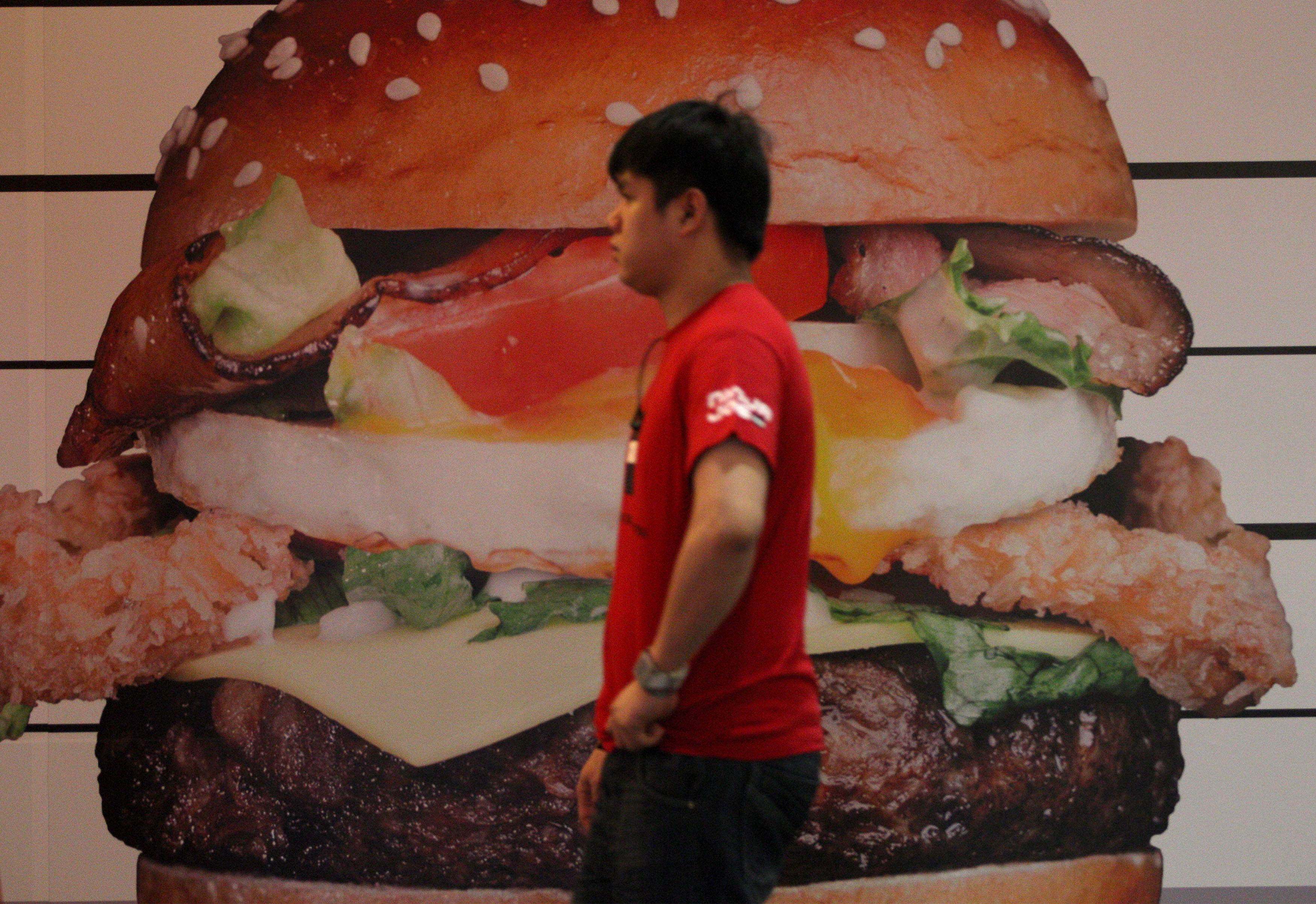 A worker walking past a burger advertisement poster inside a restaurant in Kuala Lumpur. Photo: AFP