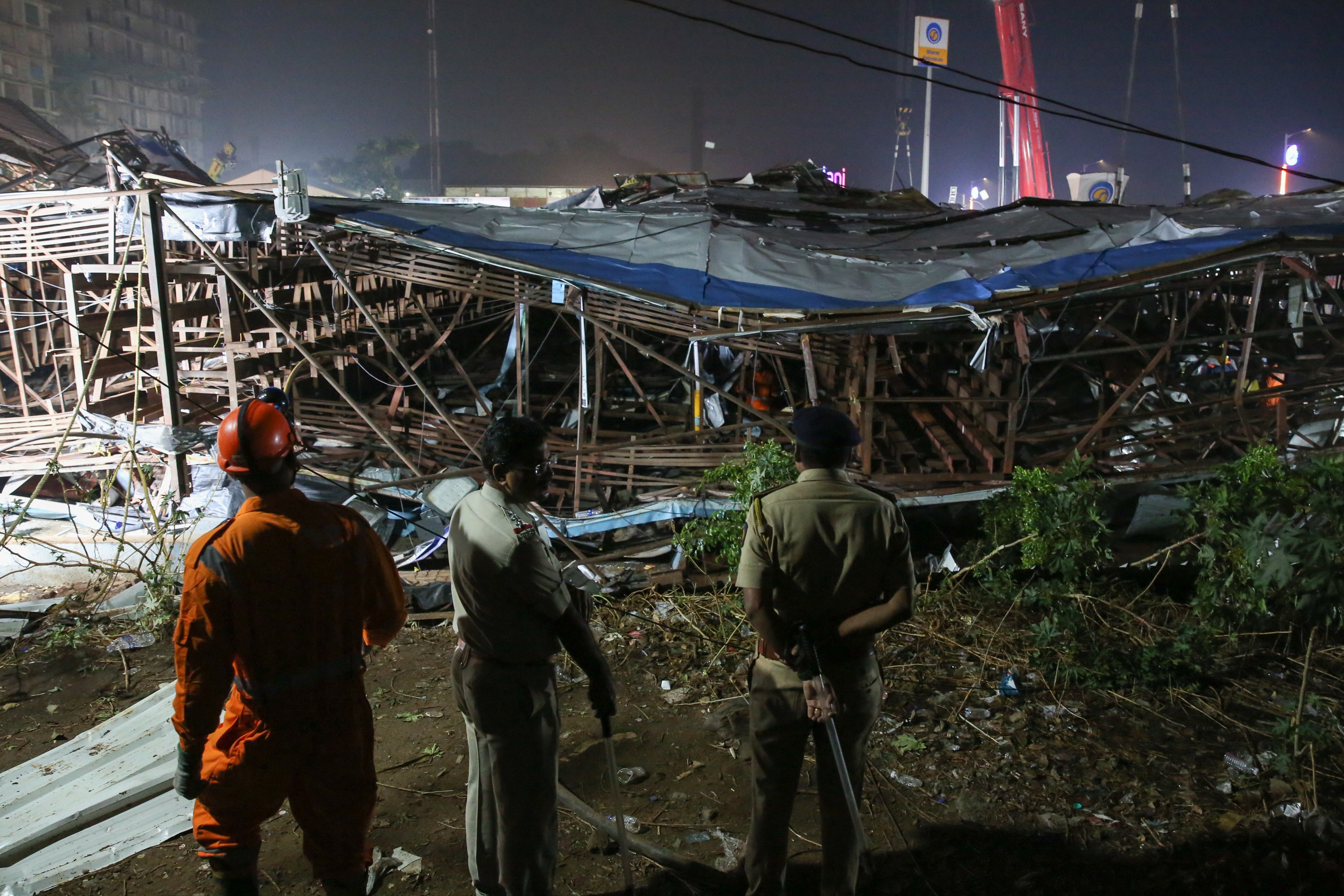 A member of the National Disaster Response Force (NDRF) and Indian policemen inspect the damages at a petrol station after a giant billboard fell on it in Mumbai, India on Monday. Photo: EPA-EFE