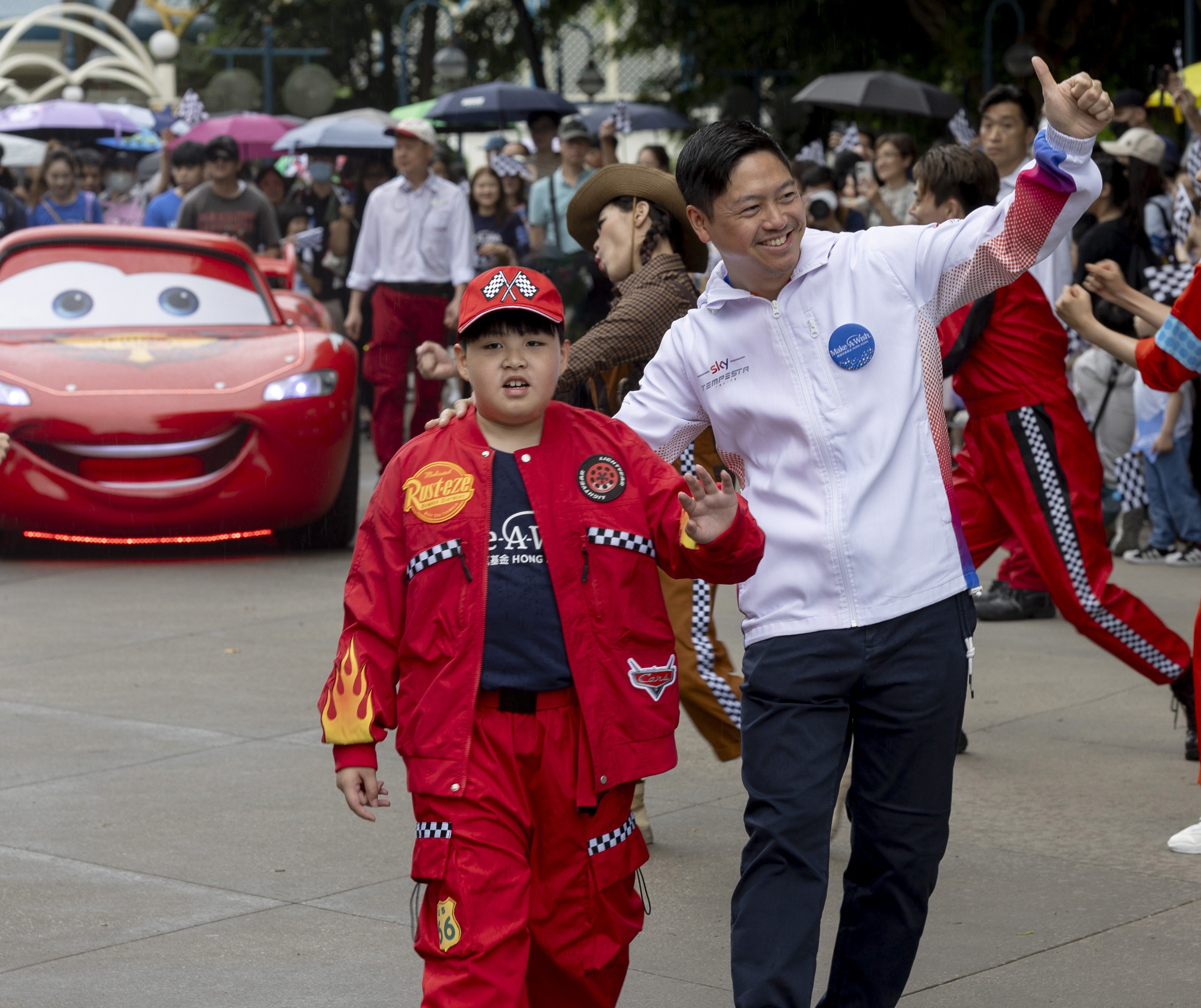 Wish child Heison Leong (left) was accompanied by Hong Kong racing driver Jonathan Hui and Disney character Lightning McQueen during a special parade at Hong Kong Disneyland Resort held in collaboration with Make-A-Wish Hong Kong to commemorate World Wish Day.