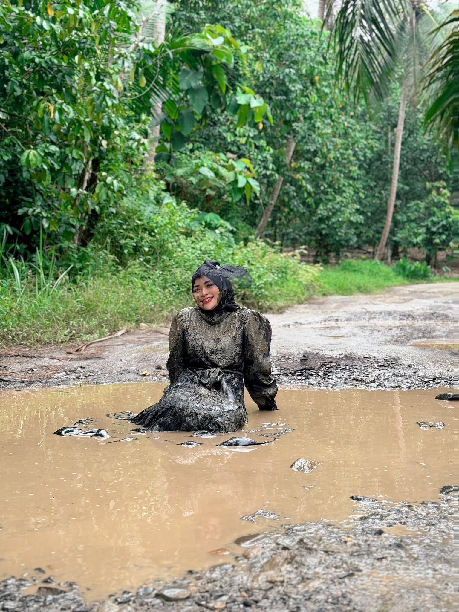 Ummu Hani sitting in mud-filled potholes on a road in Merbau Mataram, Indonesia’s southern Sumatra province. Photo: Facebook/ummuhanii
