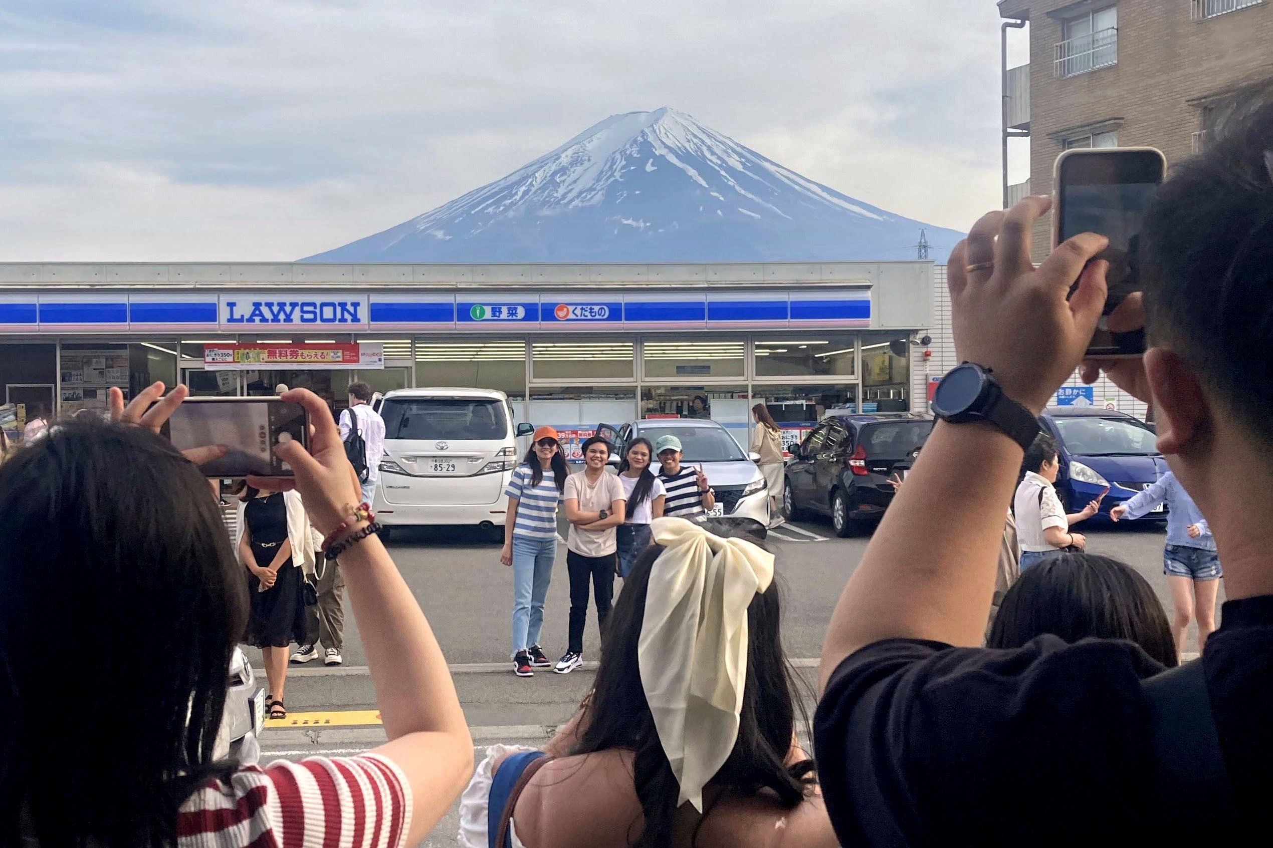 Tourists pose in front of a convenient store at Fujikawaguchiko town, Japan’s Yamanashi prefecture, with a backdrop of Mount Fuji. Photo: Kyodo News via AP