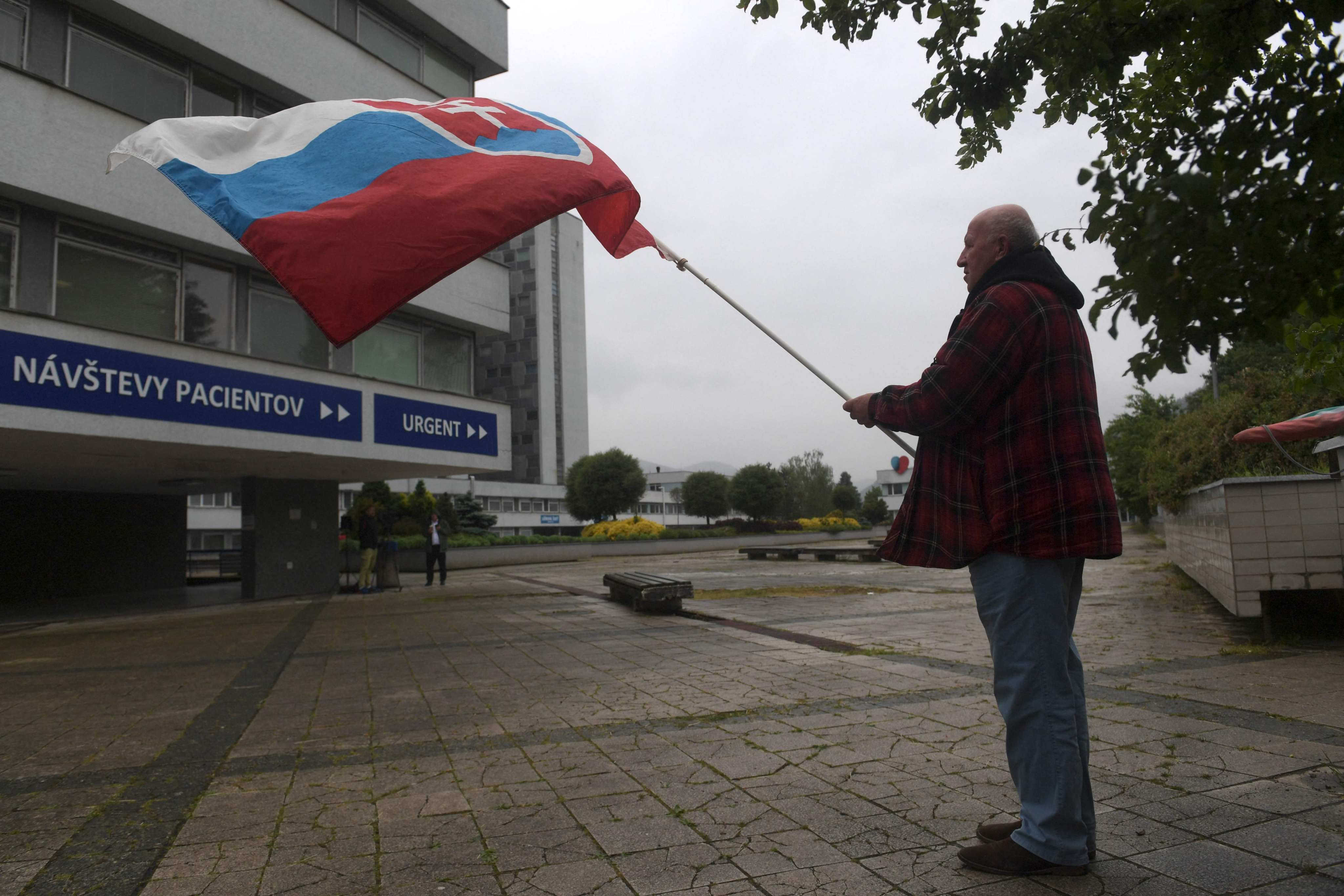 A man holds a Slovakian flag outside the hospital where Slovak Prime Minister Robert Fico is being treated on Friday. Fico had been shot “multiple times” the day before. Photo: AFP