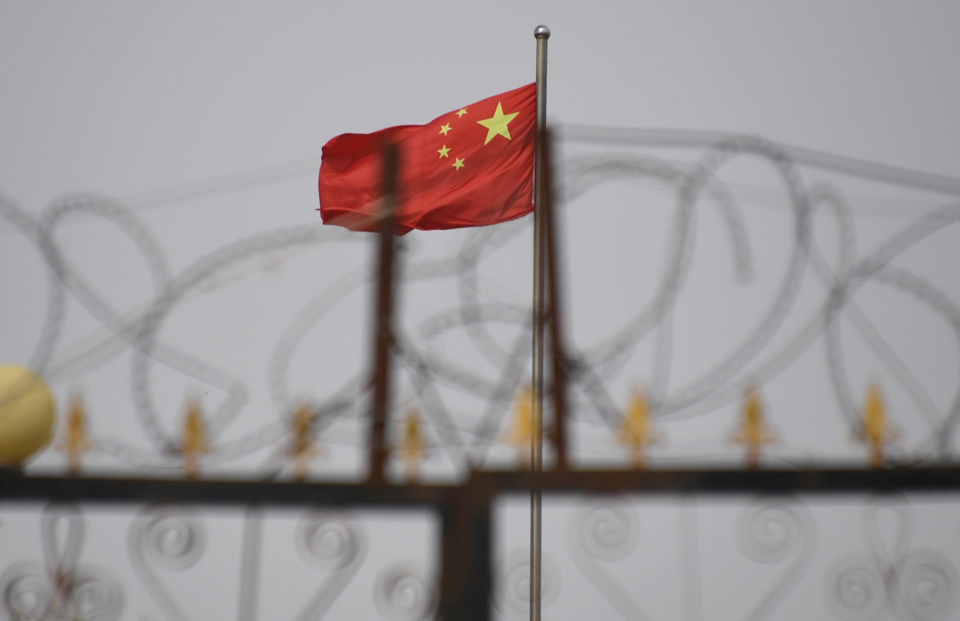The Chinese flag behind razor wire at a housing compound in Yangisar, south of Kashgar, in China’s western Xinjiang region.. PhotoL AFP/Badung Police