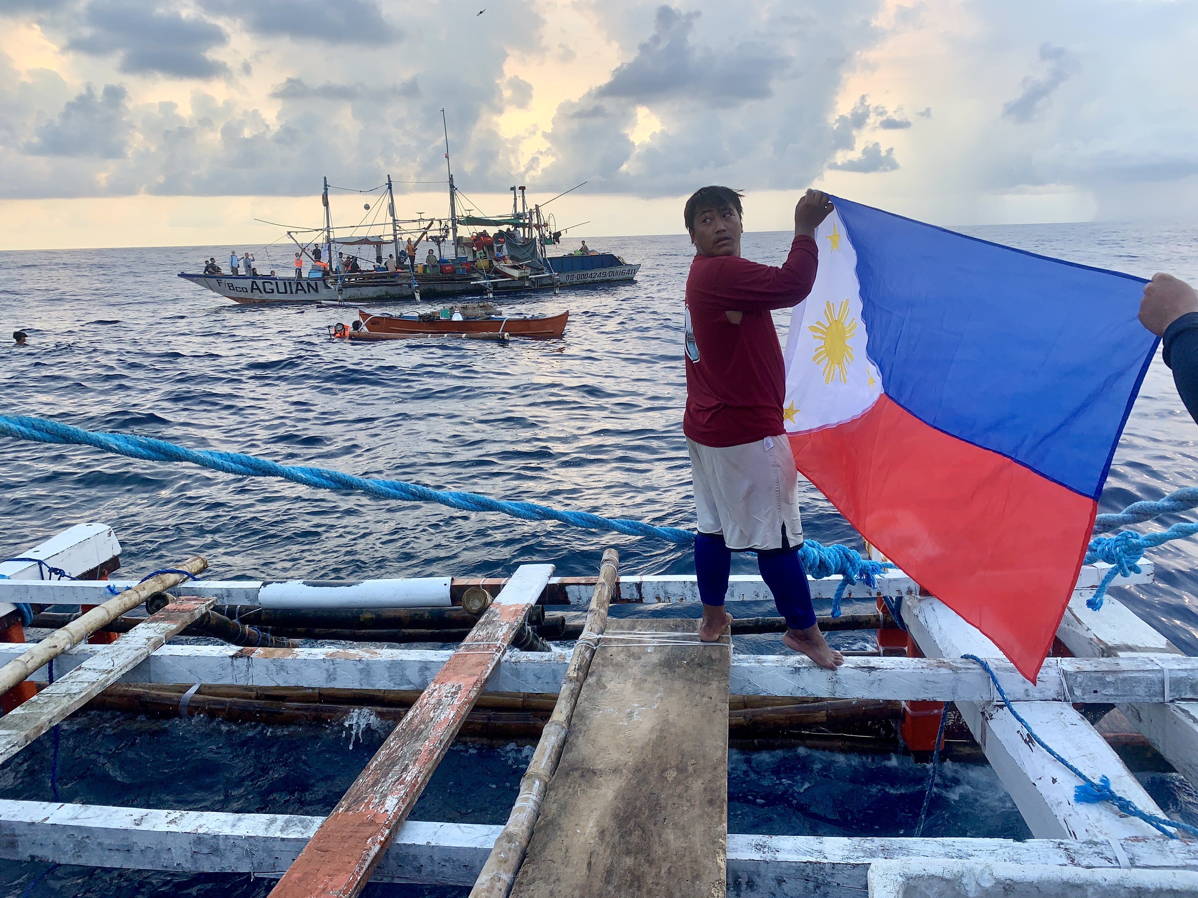 A Filipino fisherman waves a Philippine flag aboard a wooden boat as they sail towards Scarborough Shoal in the disputed South China Sea. Photo: EPA-EFE