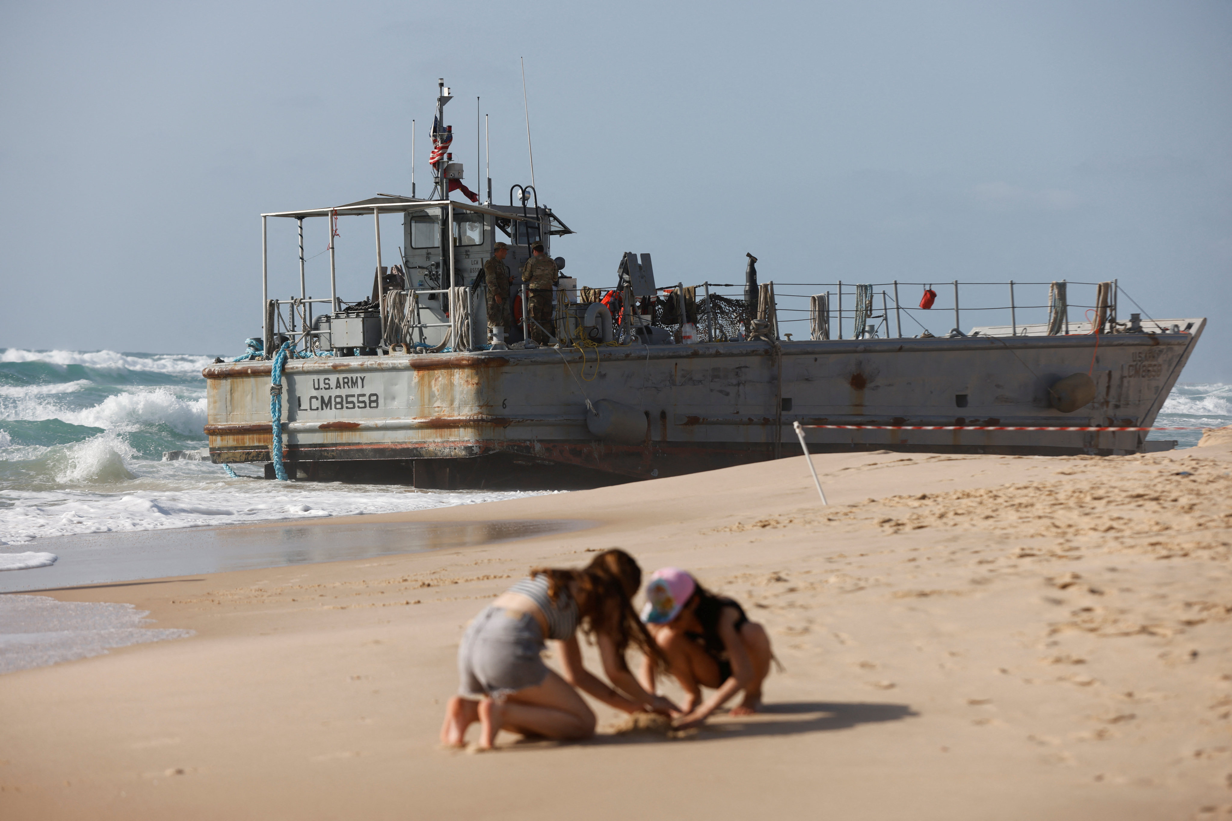 Children play in the sand as US troops work on a beached vessel in Ashdod, Israel, on Saturday. Photo: Reuters
