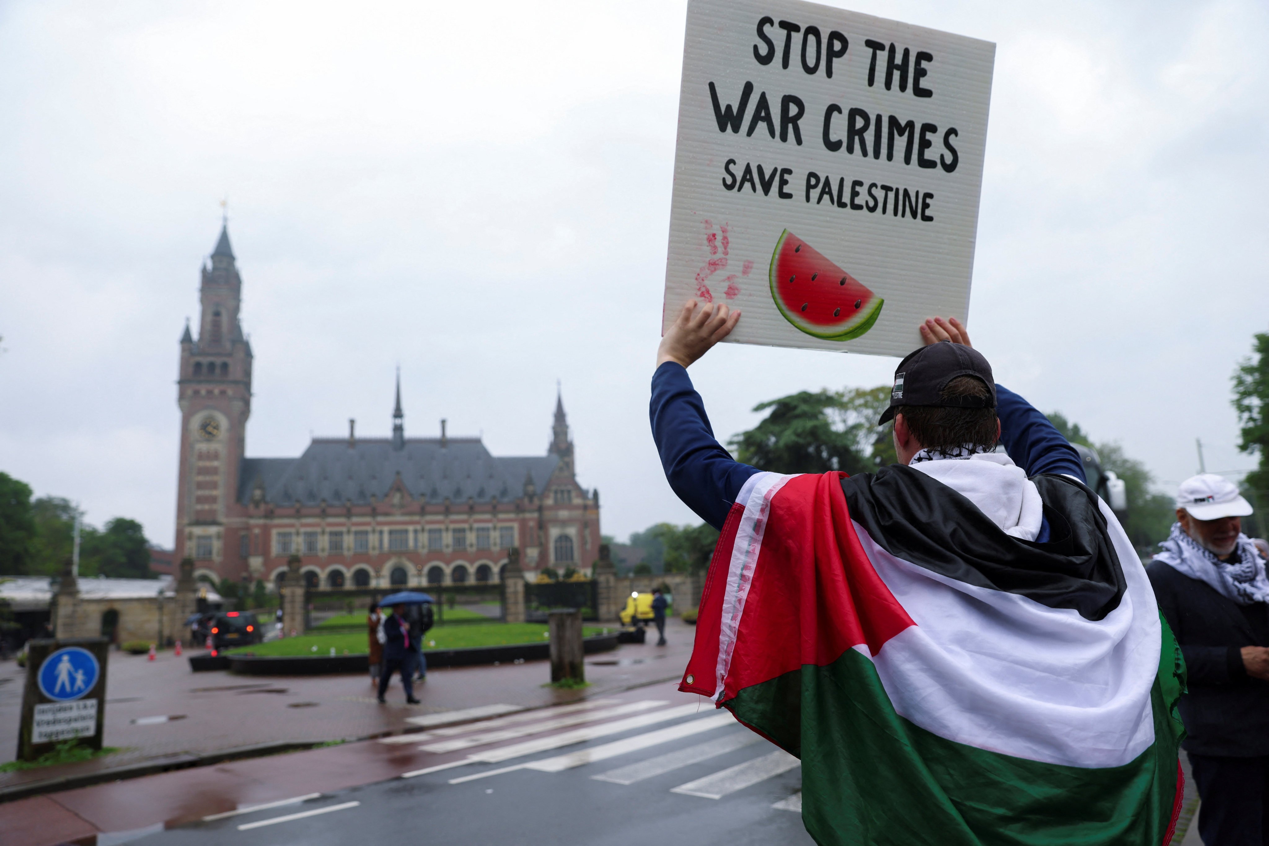 A protester draped in a Palestinian flag holds up a sign outside the International Court of Justice in The Hague on Friday. Photo: Reuters