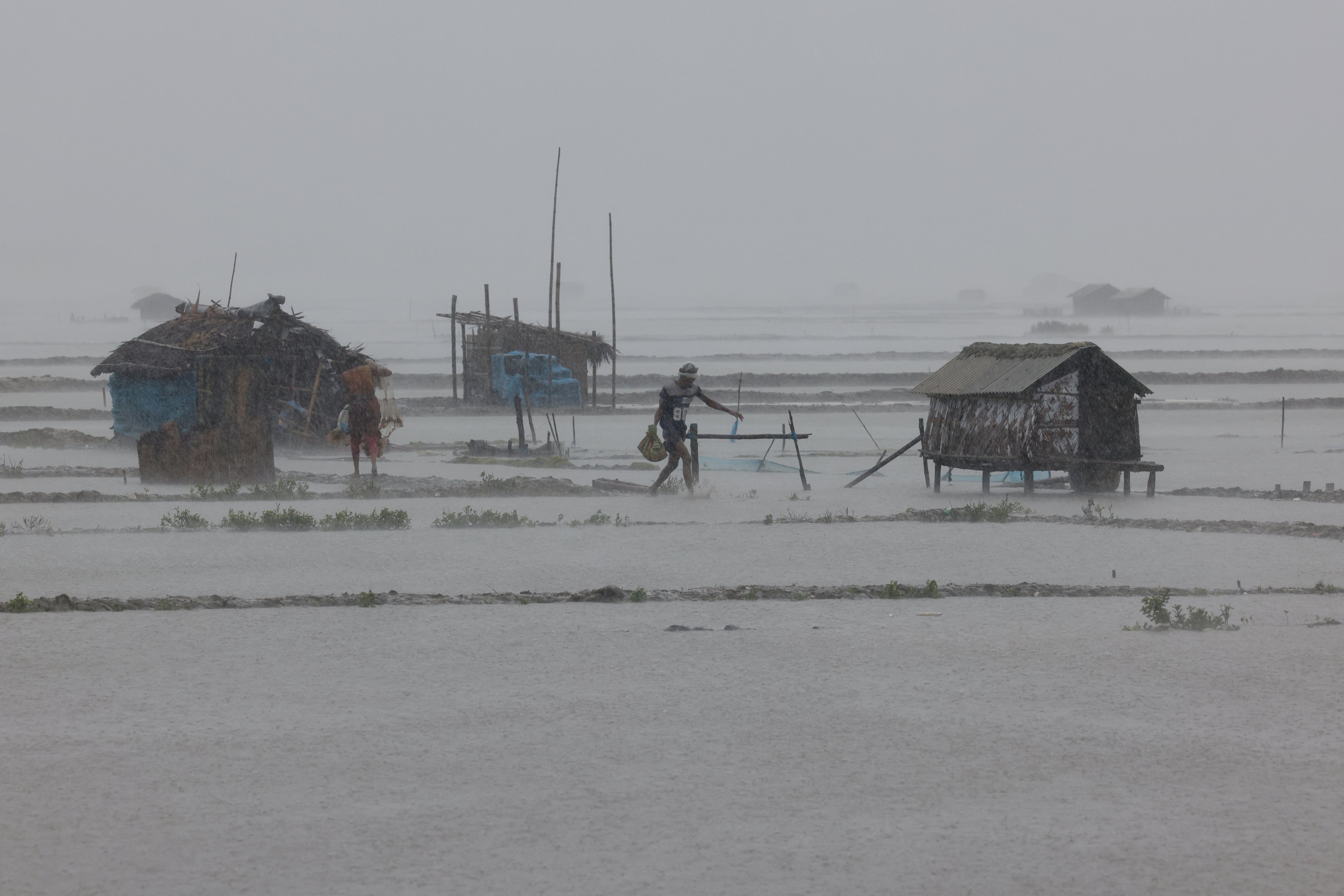 People walk through heavy rain on Monday at shrimp and crab farms in the Shyamnagar area of Satkhira, Bangladesh, as Cyclone Remal passes the country. Photo: Reuters