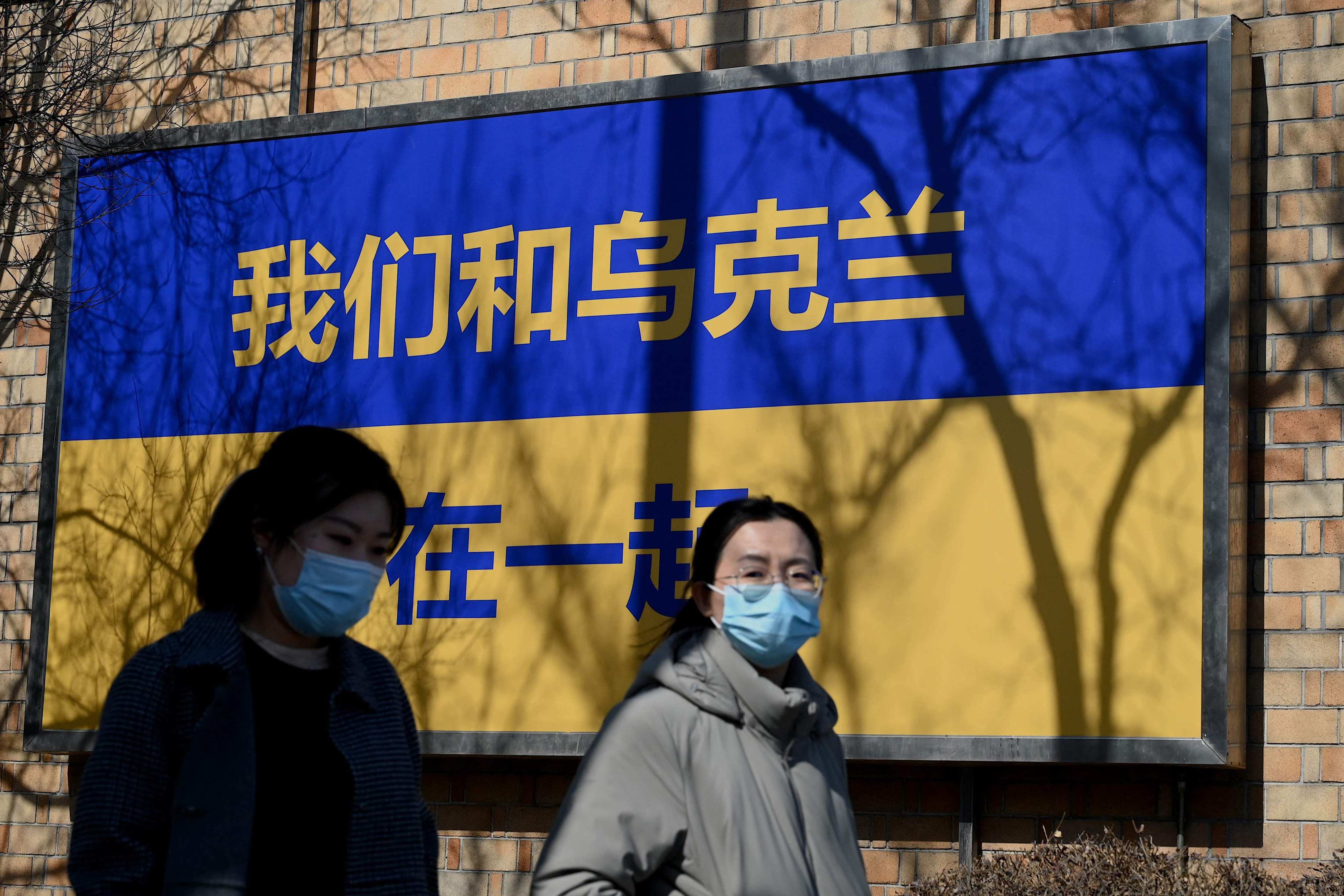Pedestrians walk past signage in the design of Ukraine’s national flag with the message, “we support Ukraine”, outside the Canadian embassy in Beijing on March 3, 2022. Photo: AFP
