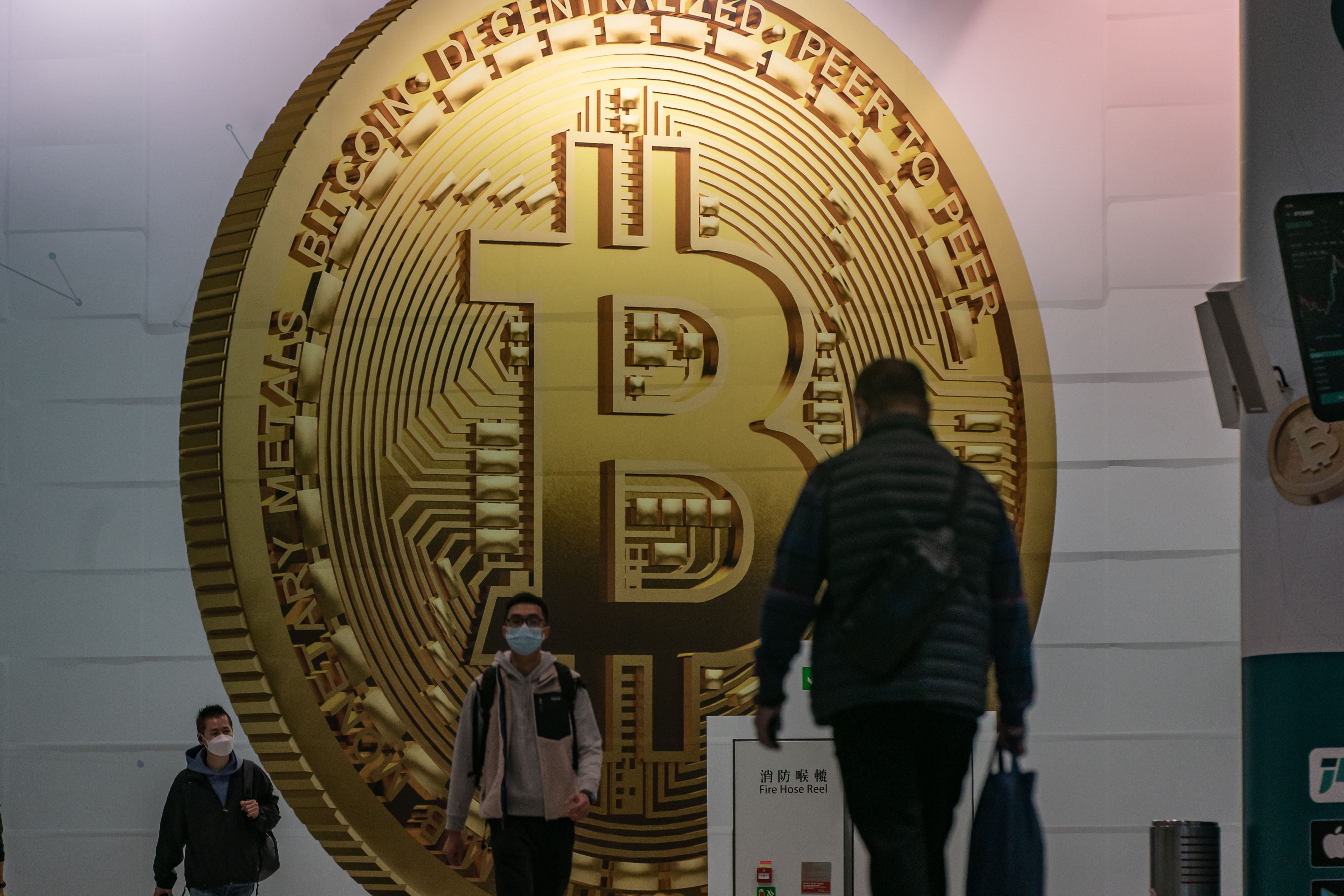 Pedestrians walk past an advertisement in Hong KOng displaying a bitcoin cryptocurrency token on February 15, 2022. Photo: Getty Images