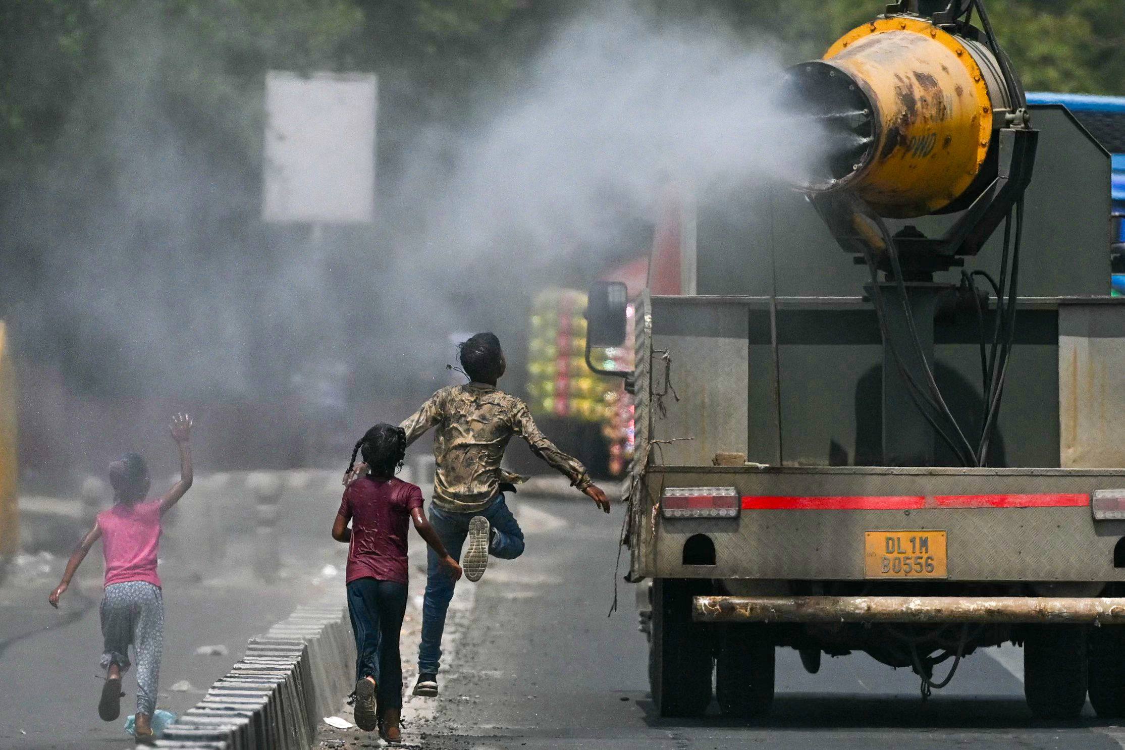 Children run behind a truck spraying water along a street on a hot summer day in New Delhi. Photo: AFP