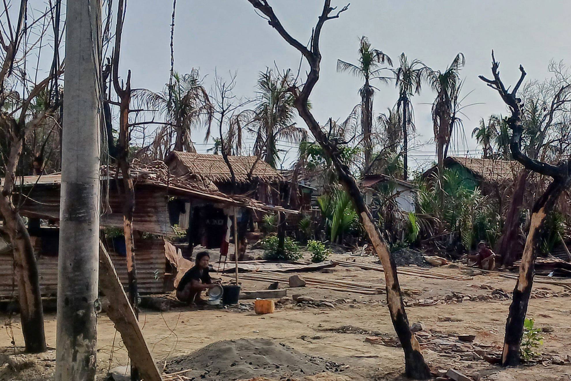 A woman cooks next to destroyed houses and burned trees following fighting between Myanmar’s military and the Arakan Army in a village in Rakhine state on May 21. Photo: AFP