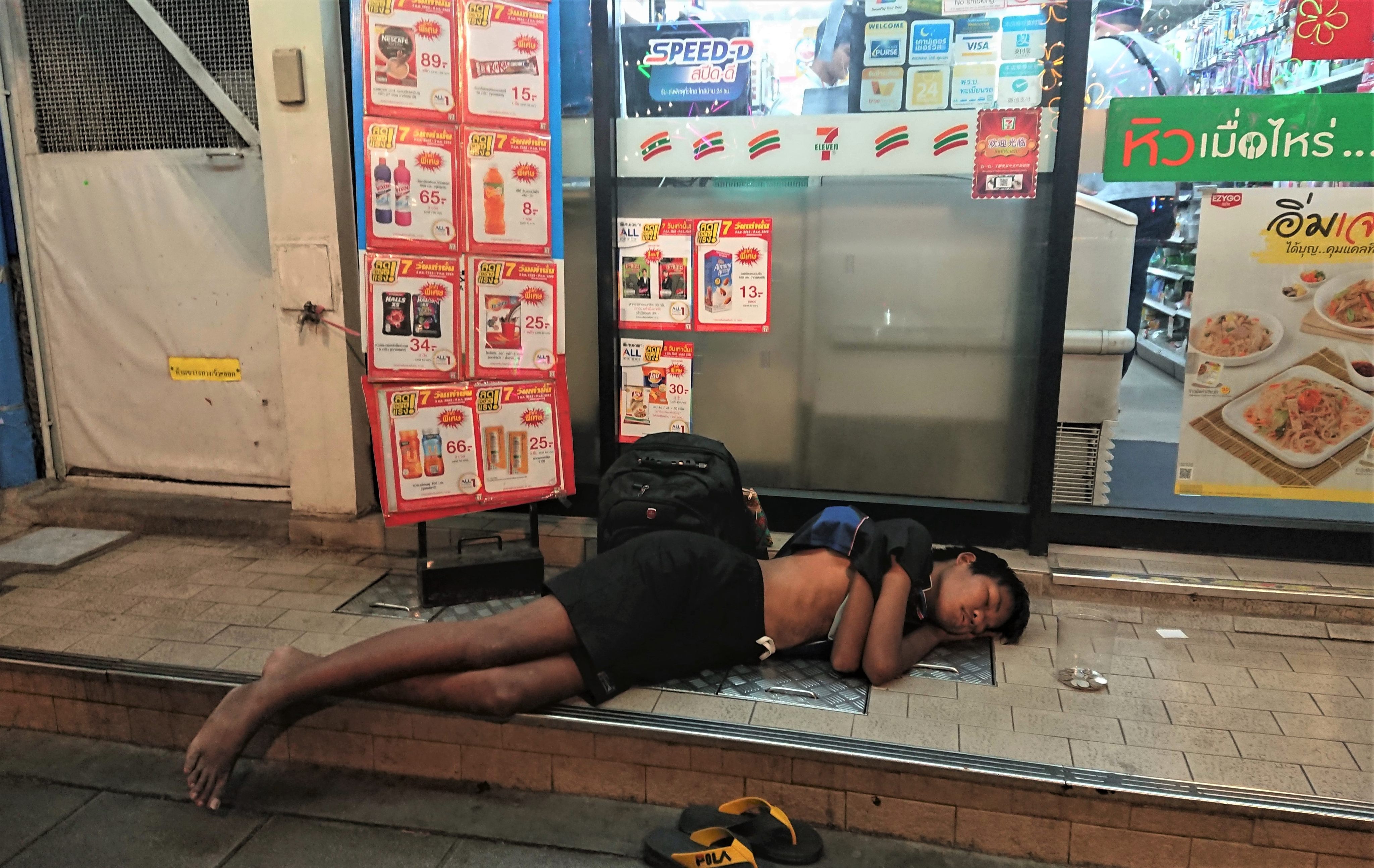 A boy sleeps outside a 7-Eleven store near Siam Square in central Bangkok where he begs most evenings. Photo: Tibor Krausz