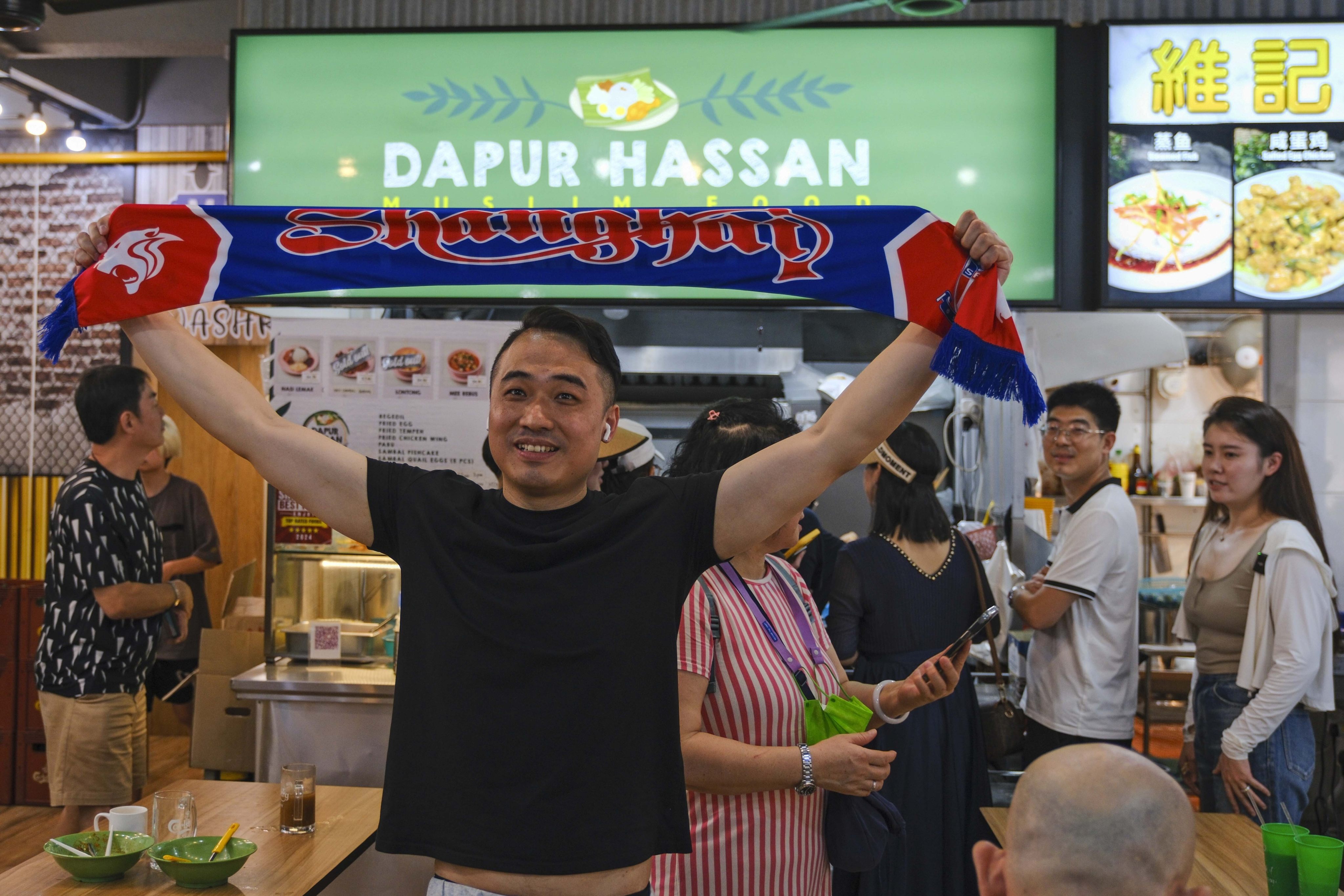 A Chinese football fan in front of Singaporean goalkeeper Hassan Sunny’s food stall in Singapore on Friday. Photo: AP