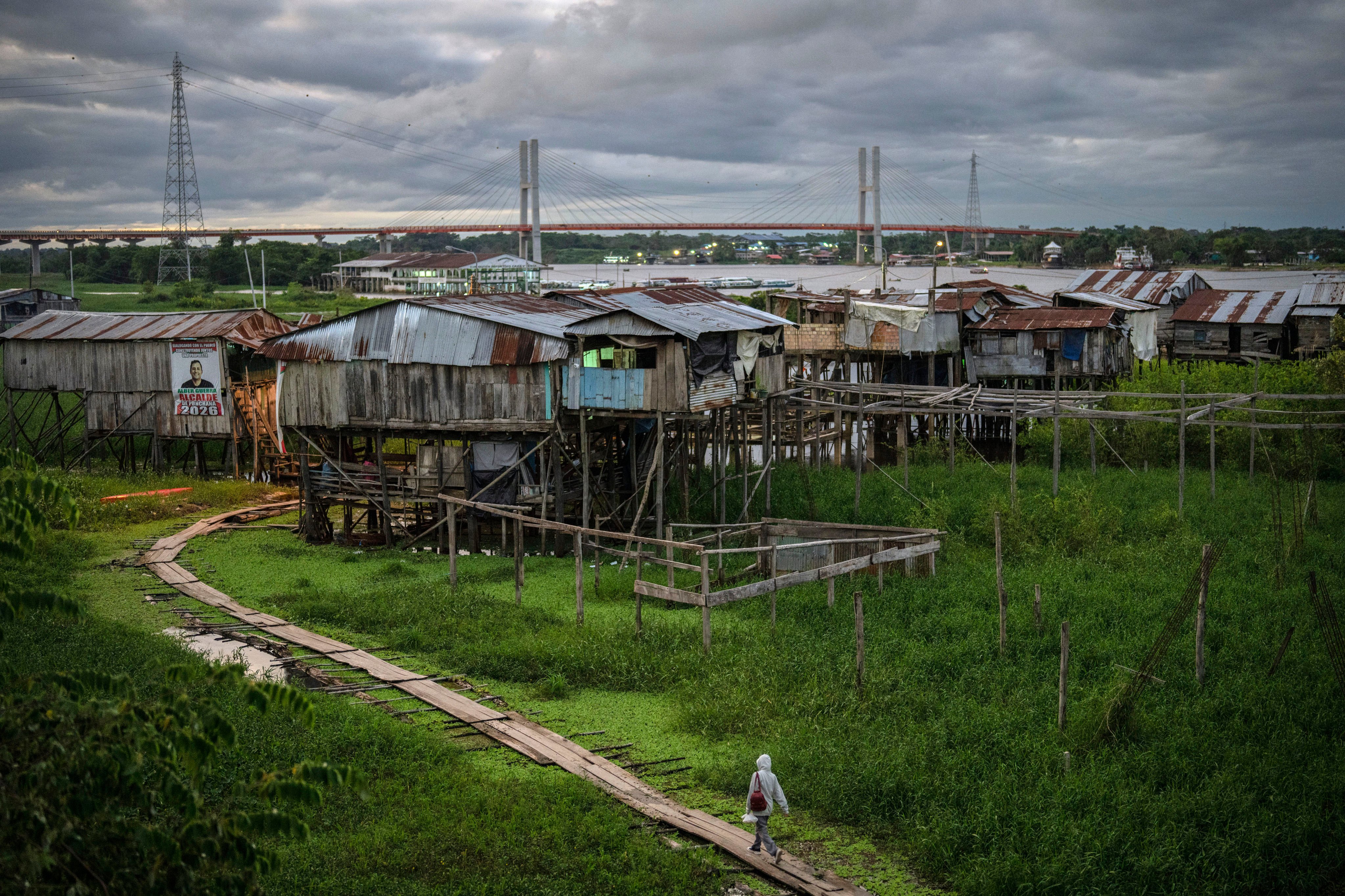 A highway bridge (in background) that is part of a federal highway project, extends across the Nanay River as a resident walks along a boarded path in the Punchana district of Iquitos, Peru. Photo: AP