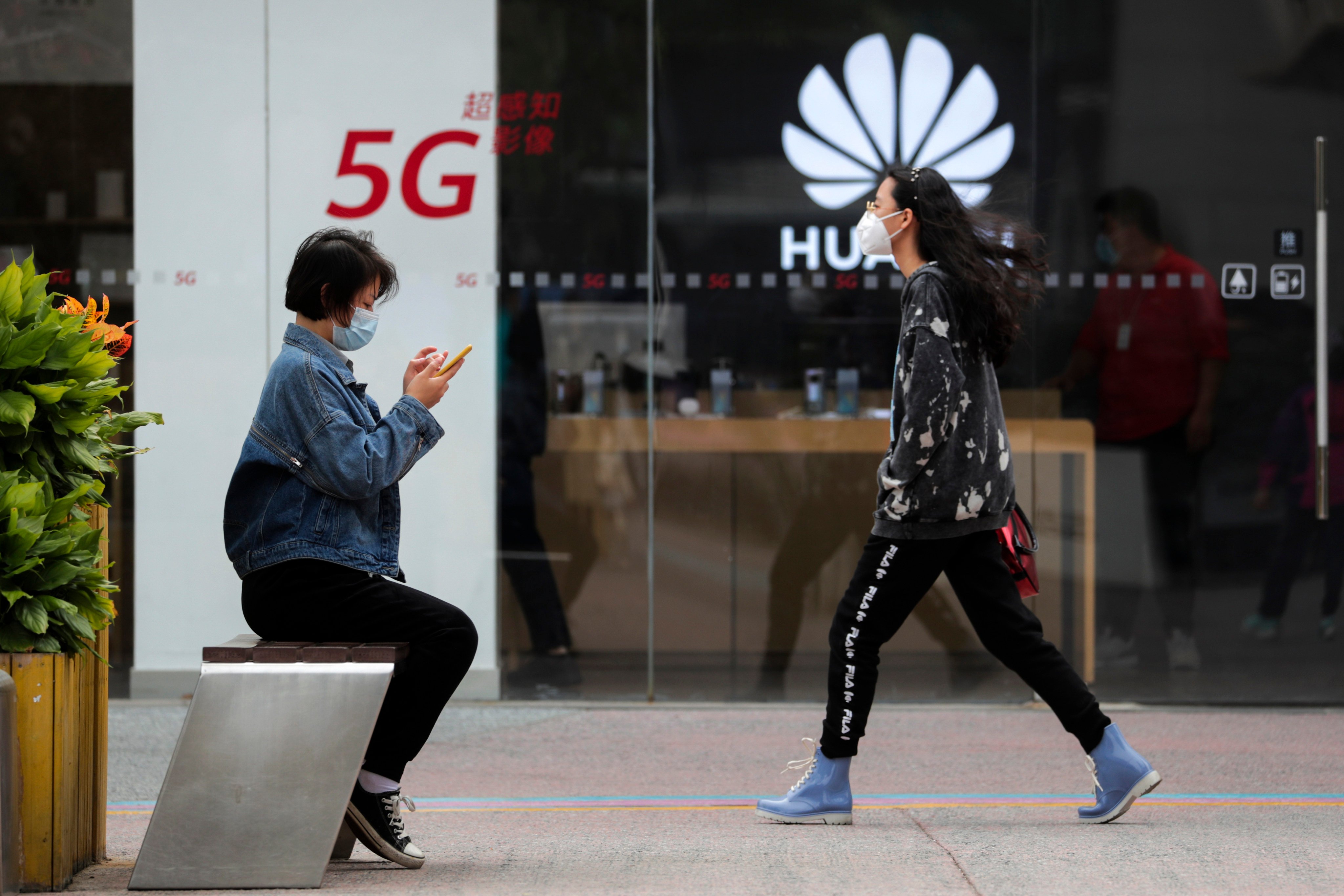 In this Oct. 11, 2020, file photo, a woman browses her smartphone as a woman walks by the Huawei retail shop promoting its 5G network in Beijing. Photo: AP