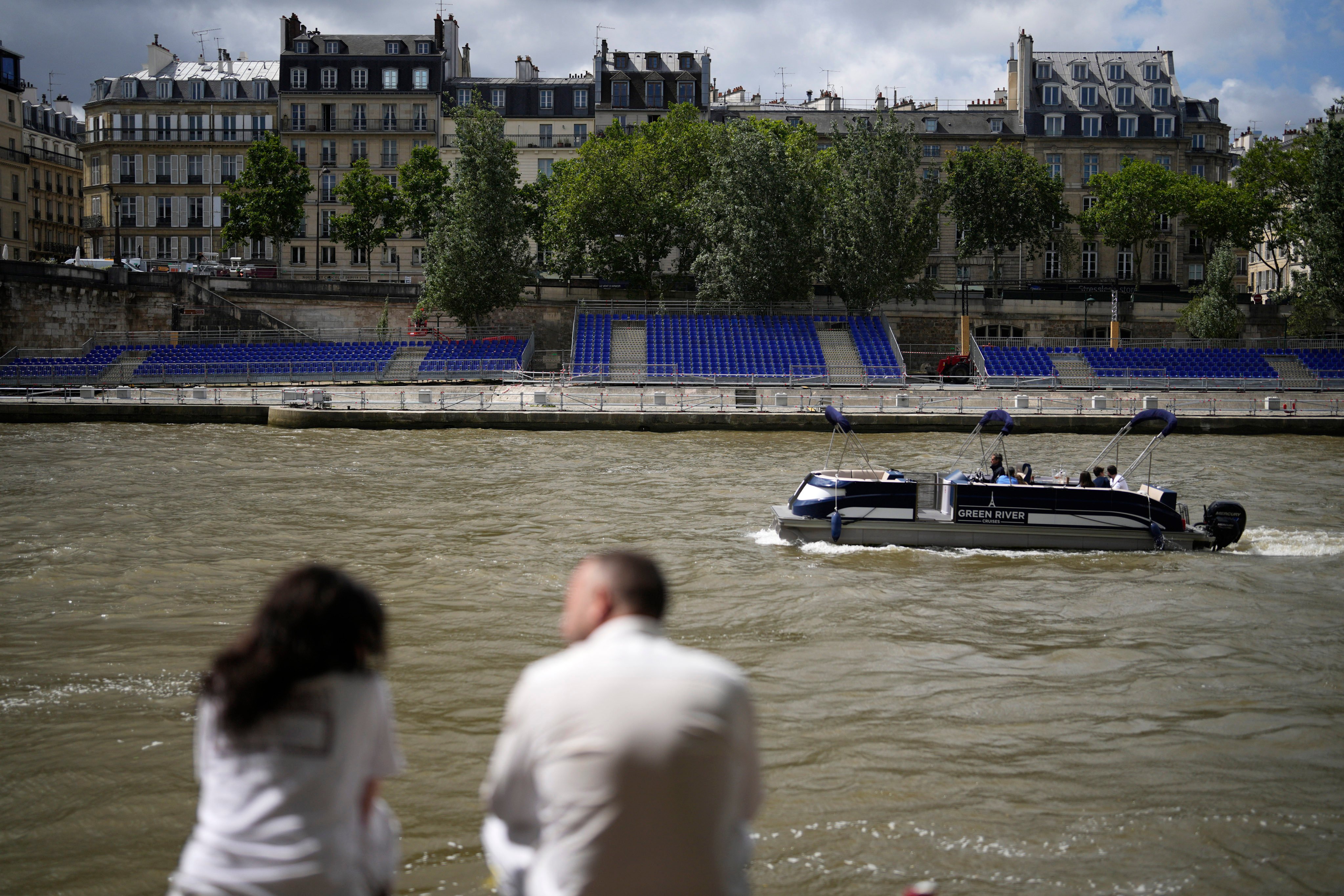 People sit along the Seine River with stands installed on its banks. The river will host the Paris Olympic Games opening ceremony on July 26. Photo: AP