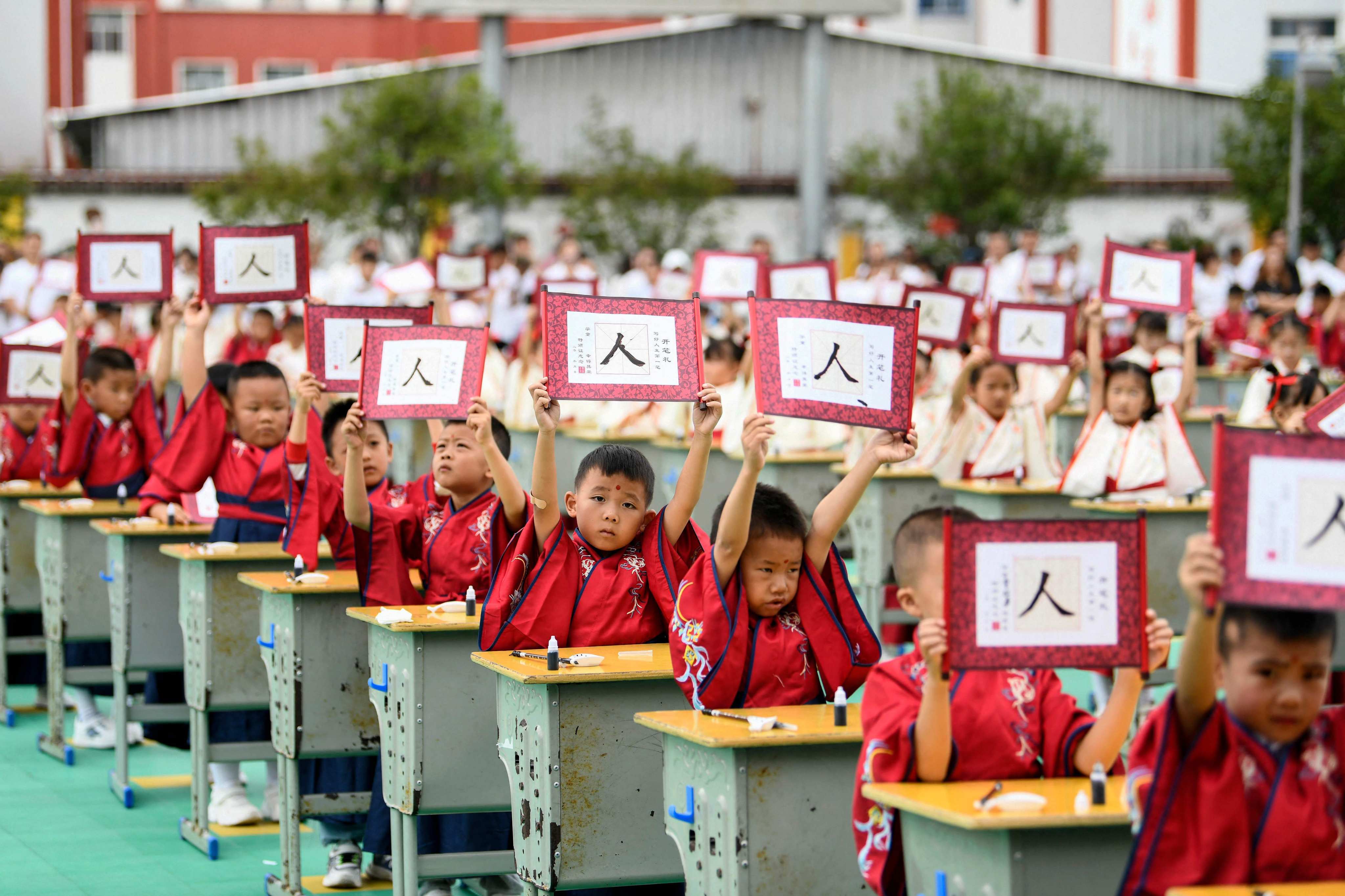 First-grade students wearing Hanfu clothing hold up cards with the character ‘ren’ meaning ‘person’ during a ceremony to learn about traditional culture at a primary school in Anlong County, Guizhou province, August 28, 2023. Photo: AFP