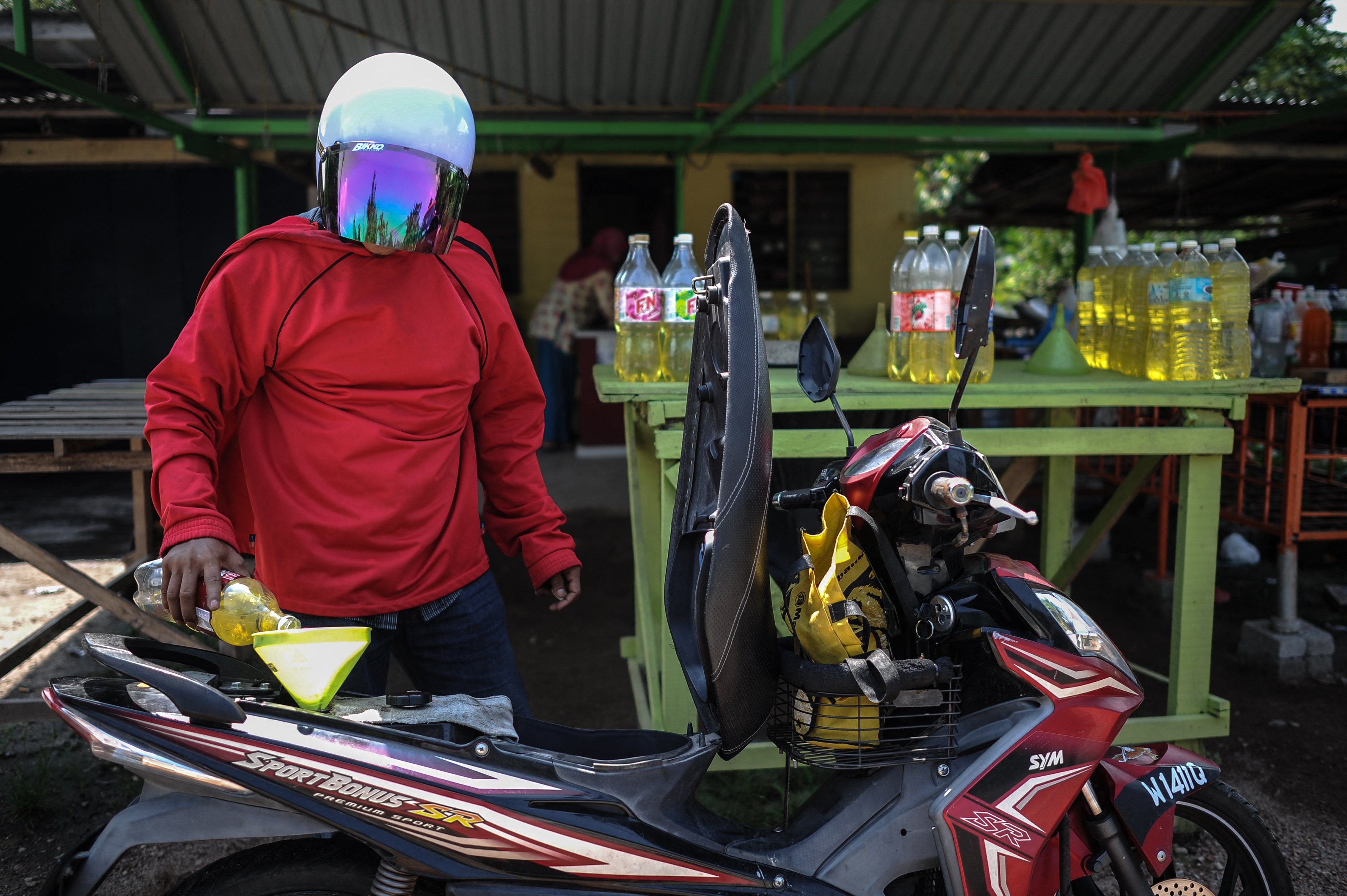 A man pours petrol from a bottle into the fuel tank of a moped in a village on the outskirts of Kuala Lumpur. Photo: AFP