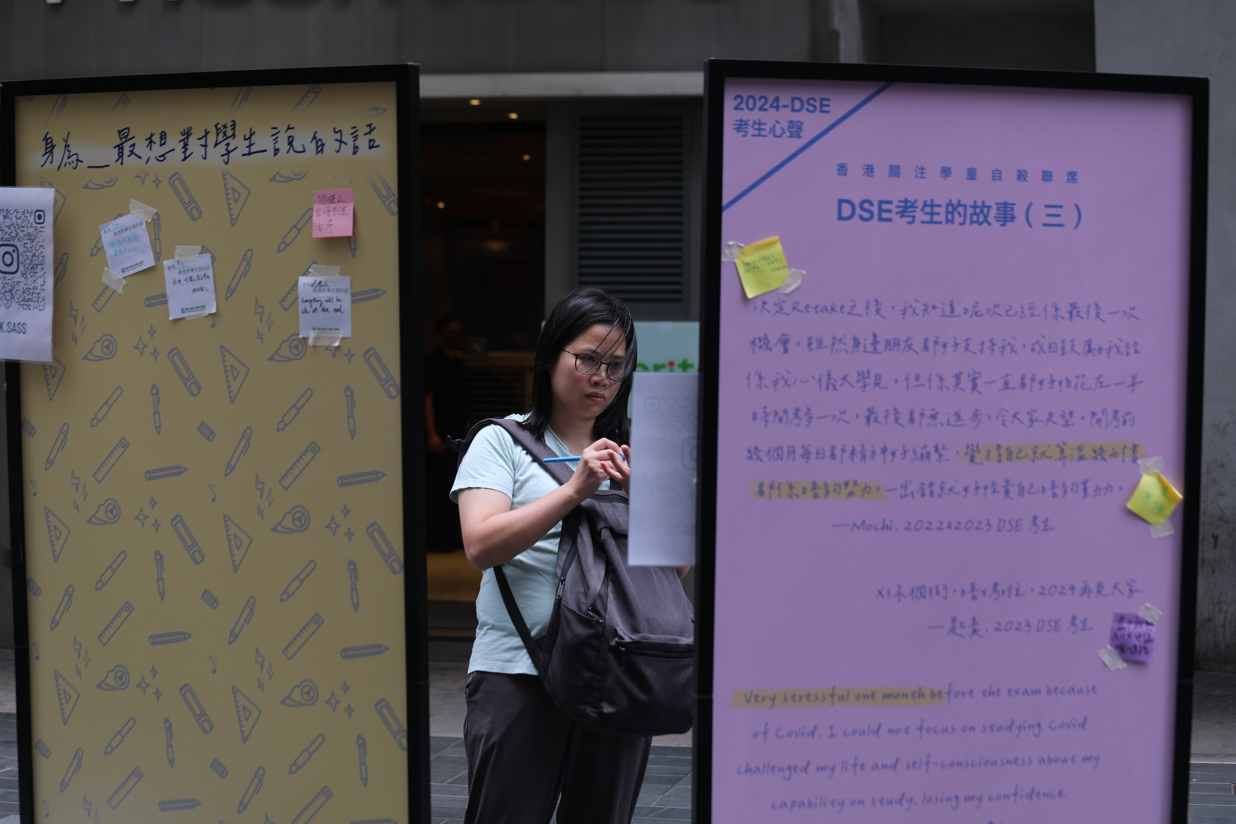 A passerby writes a note to students taking the Diploma of Secondary Education exam on boards put up as part of a suicide prevention campaign by a student group in Causeway Bay on May 18.  Photo: Xiaomei Chen