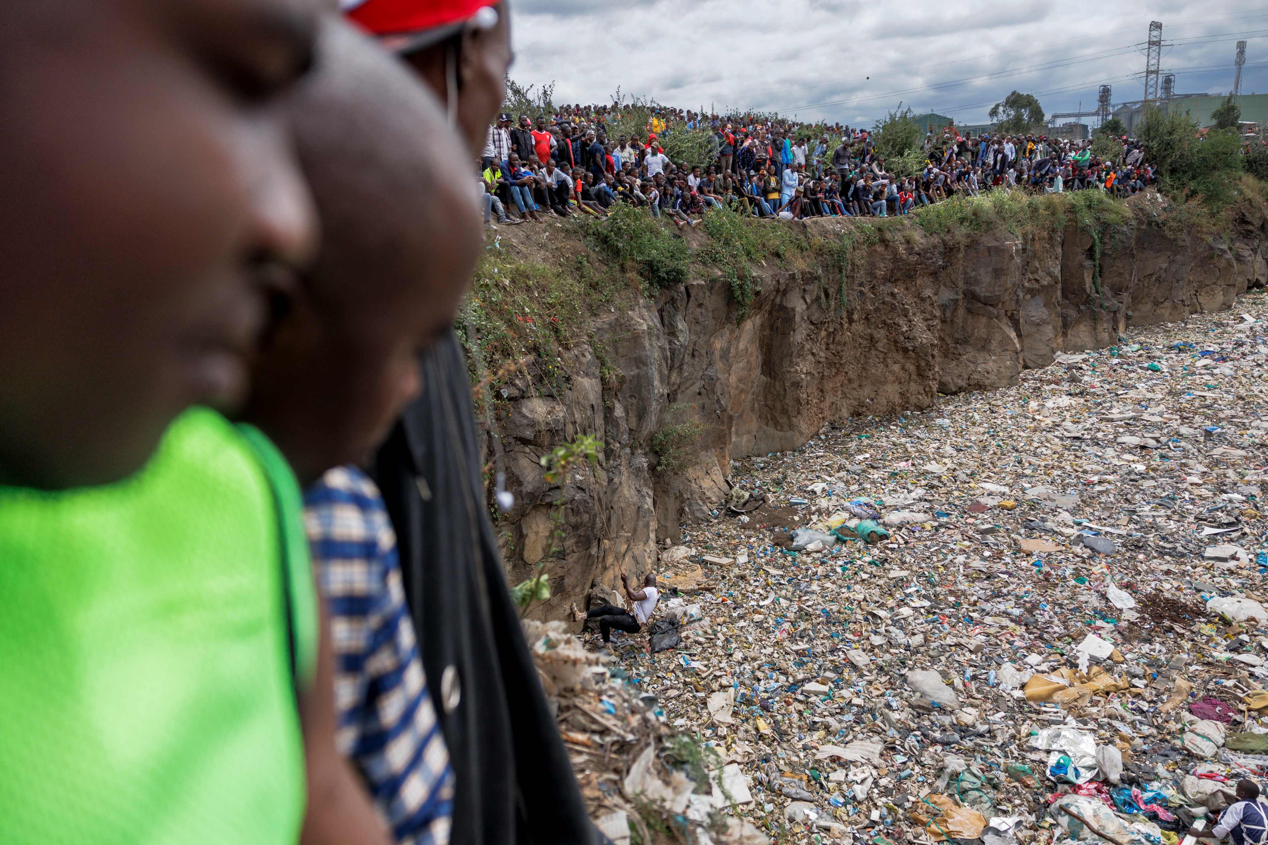 Crowds gather on the edge of an abandoned quarry to watch volunteers searching through a rubbish dump for human remains at Mukuru slum. Photo: AFP