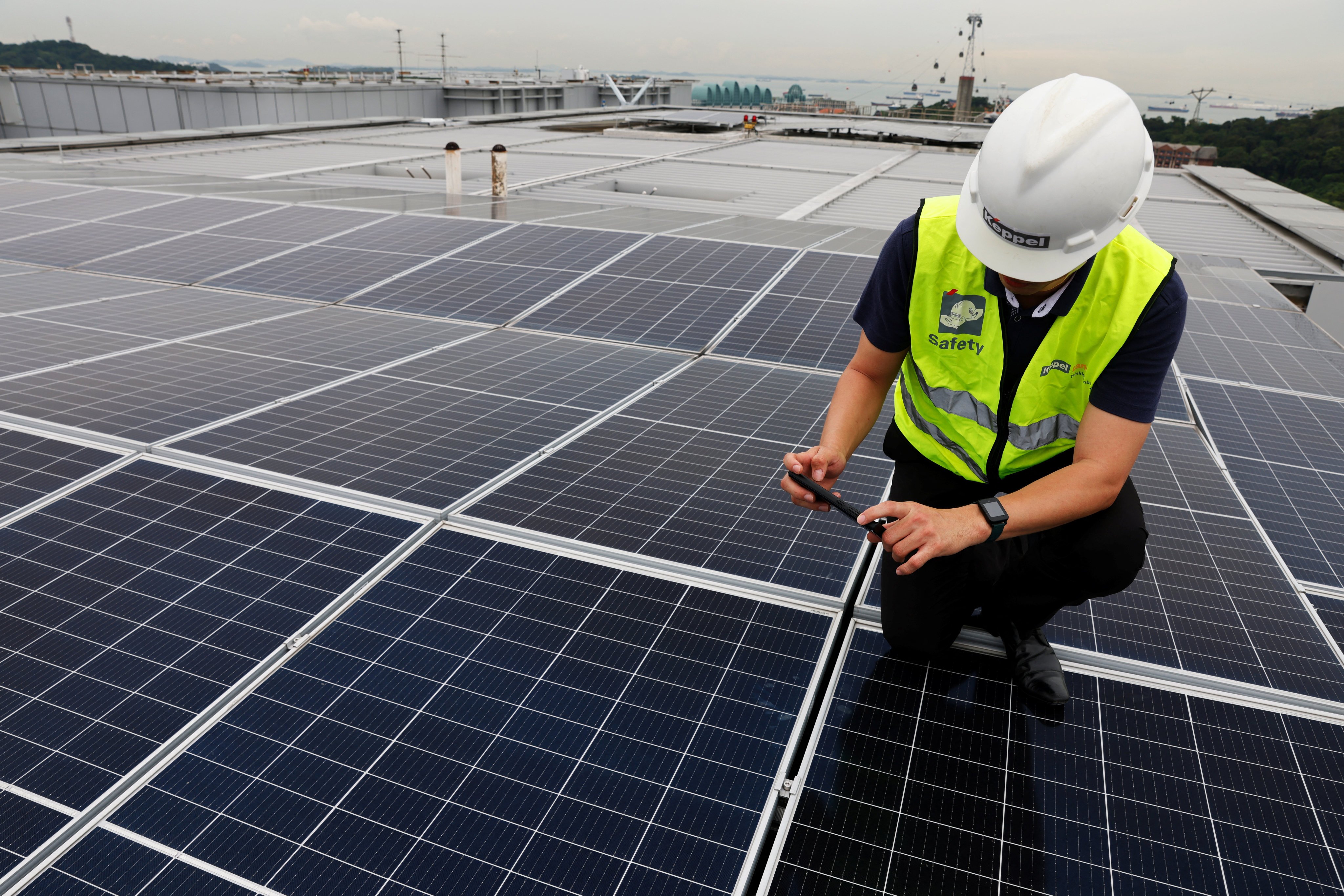 An energy company employee kneels on rooftop solar panels in Singapore on July 6, 2023. Sharing expertise with other countries and even collaboration among business competitors can help boost sustainability efforts throughout the region. Photo: Reuters