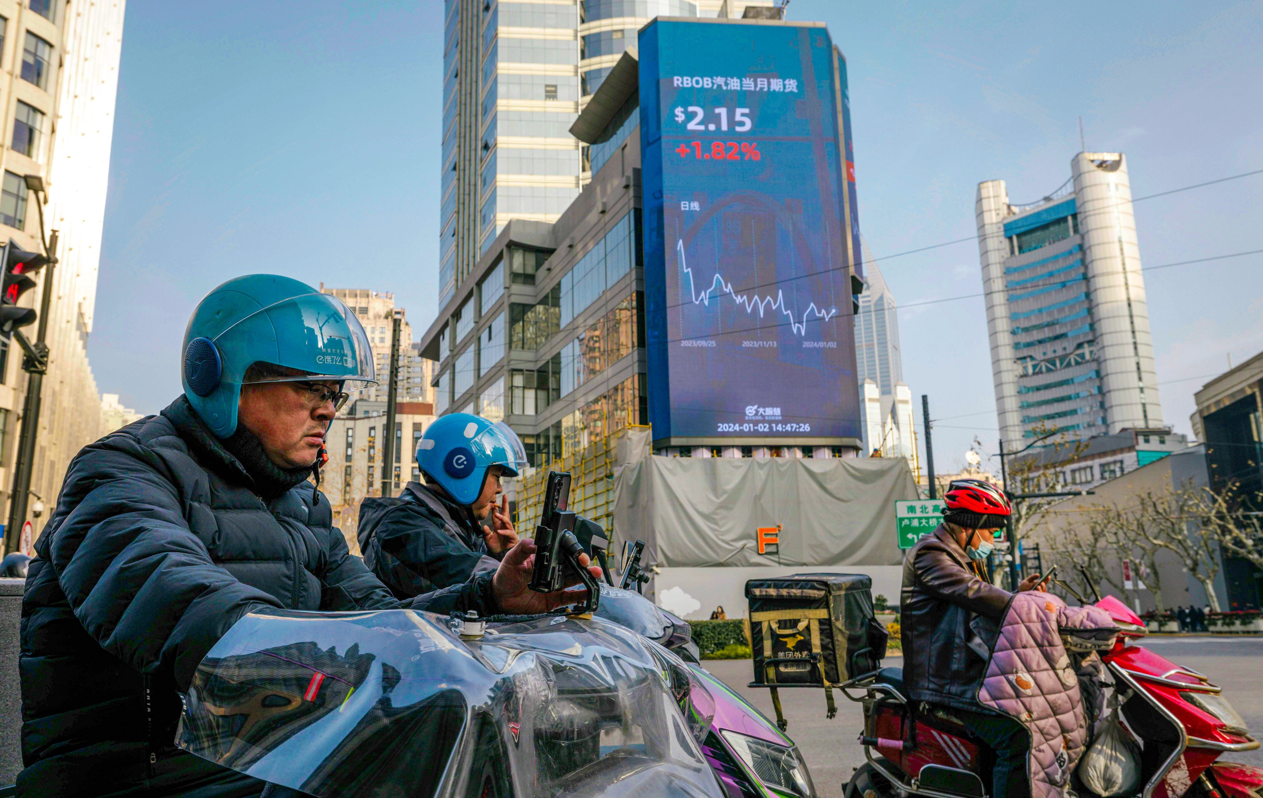 People ride scooters on the street beneath a large screen showing the latest stock data in Shanghai on January 2, 2024. Photo: EPA-EFE