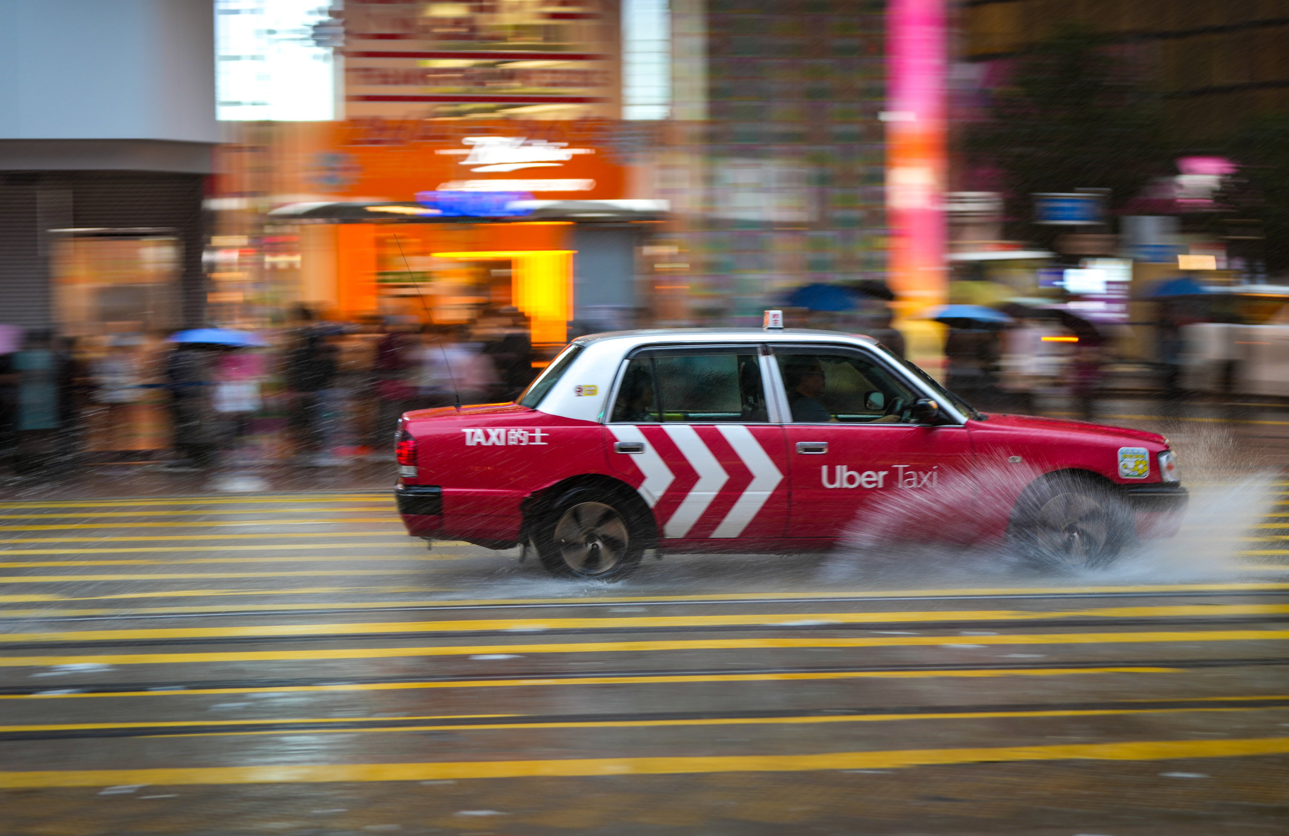 A taxi with the an ad for Uber splashes through water on the street during a rainstorm in Causeway Bay on May 21. While some taxi drivers have signed up for the ride-hailing platform, a large number are opposed to it operating in Hong Kong. Photo: Sam Tsang