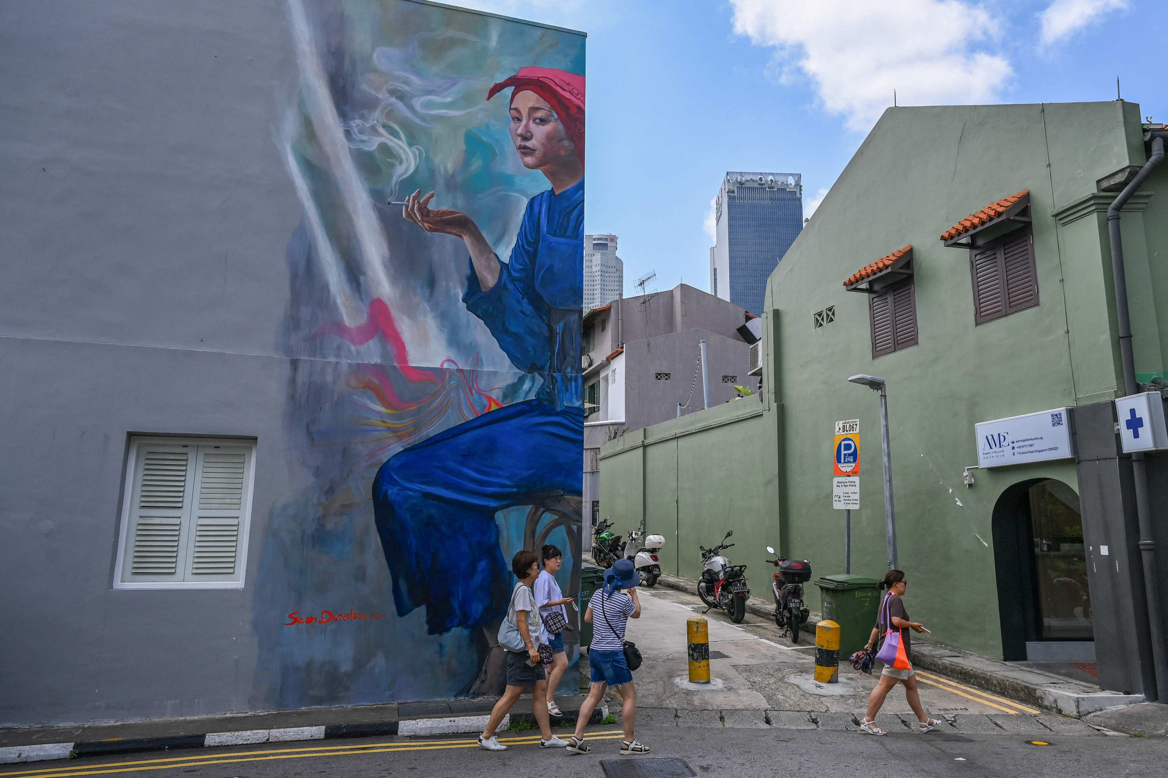 People walk past a mural by artist Sean Dunston of a Samsui woman holding a cigarette on the side of a building in the Chinatown district of Singapore. Photo: AFP