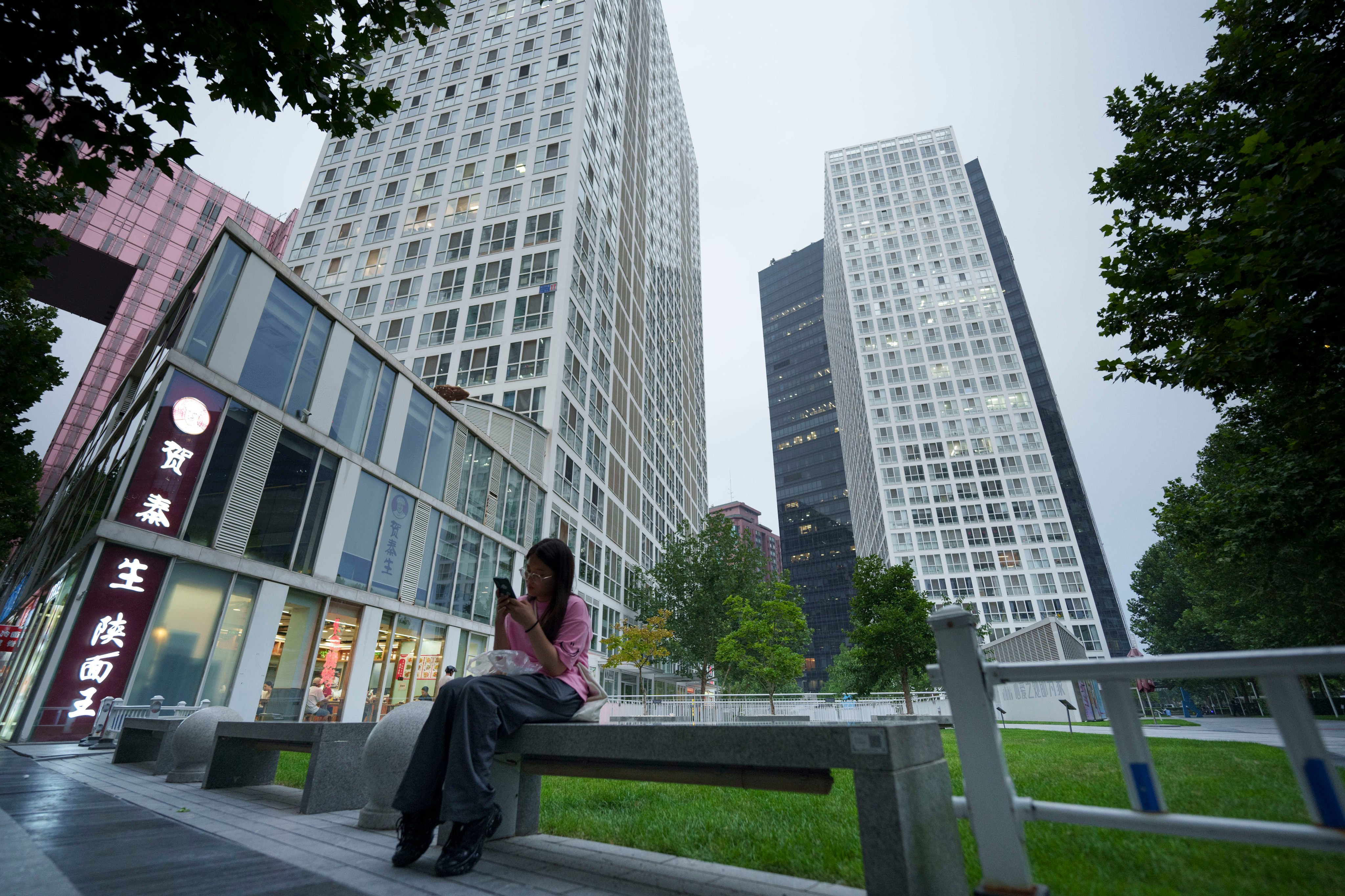 A woman rests on a bench near office buildings around the central business district in Beijing on July 15. The office market in China and elsewhere in Asia faces new challenges as occupier and investment demand focuses on premium buildings. Photo: AP