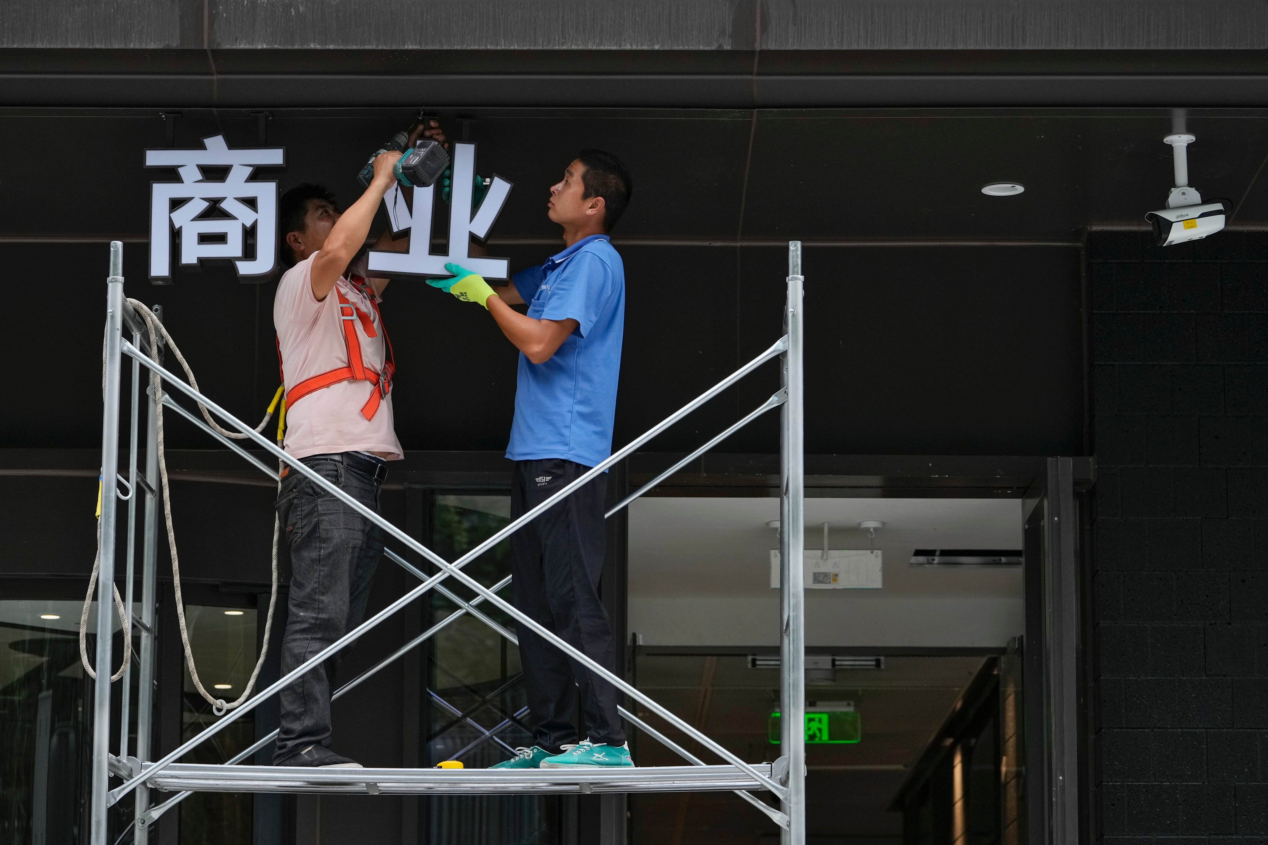 Workers on a scaffolding install a sign that reads “commerce” on a commercial office building in Beijing. Photo: AP