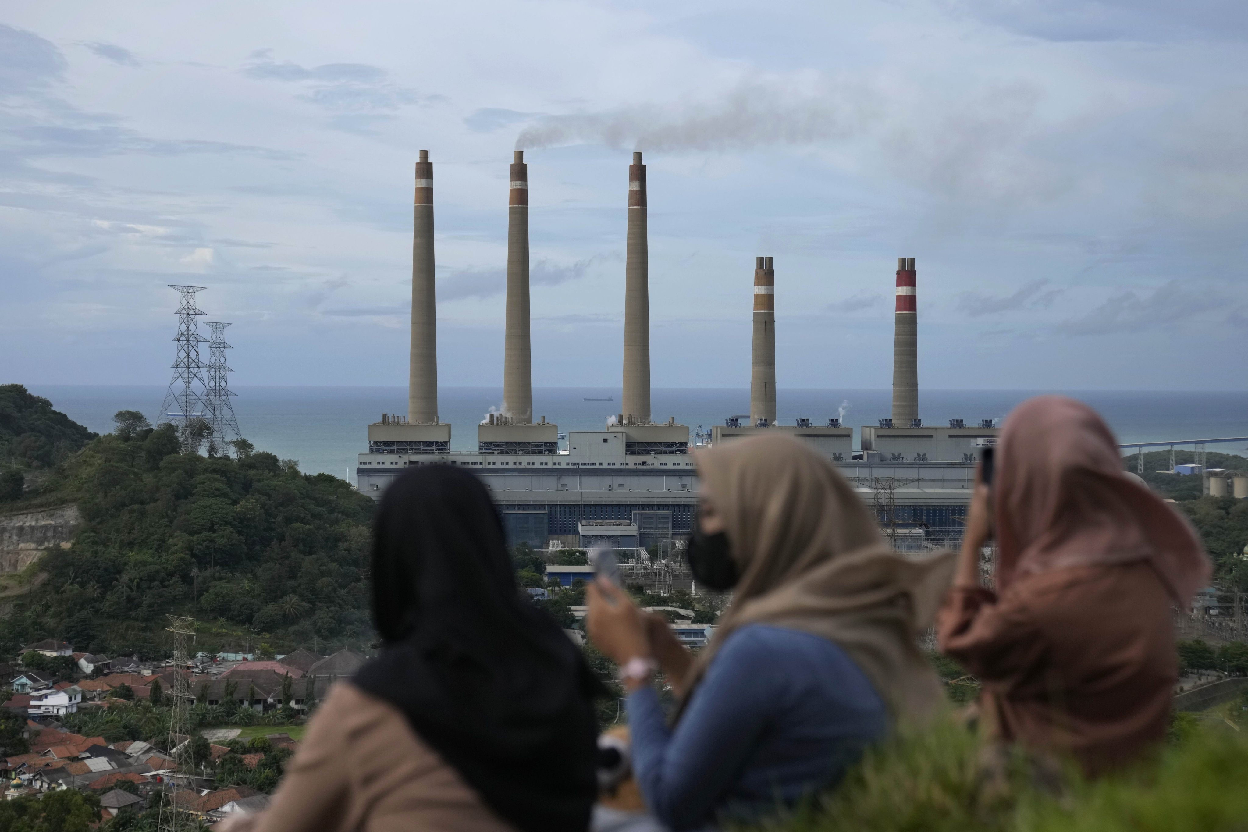 Women take photographs of a coal power plant from a hill in Cilegon, Indonesia, on January 8, 2023. Photo: AP