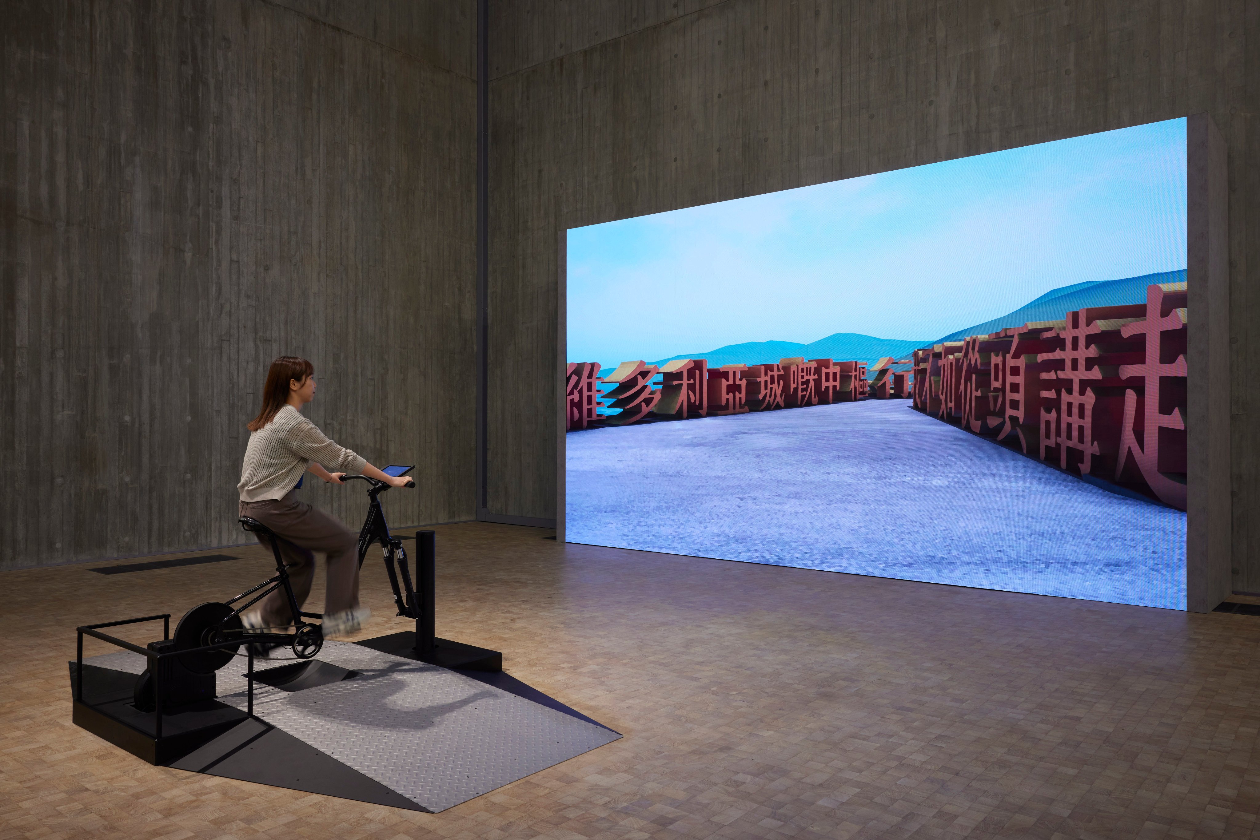 A player rides a stationary bicycle to navigate through artwork Legible City Hong Kong at M+. Photo: M+