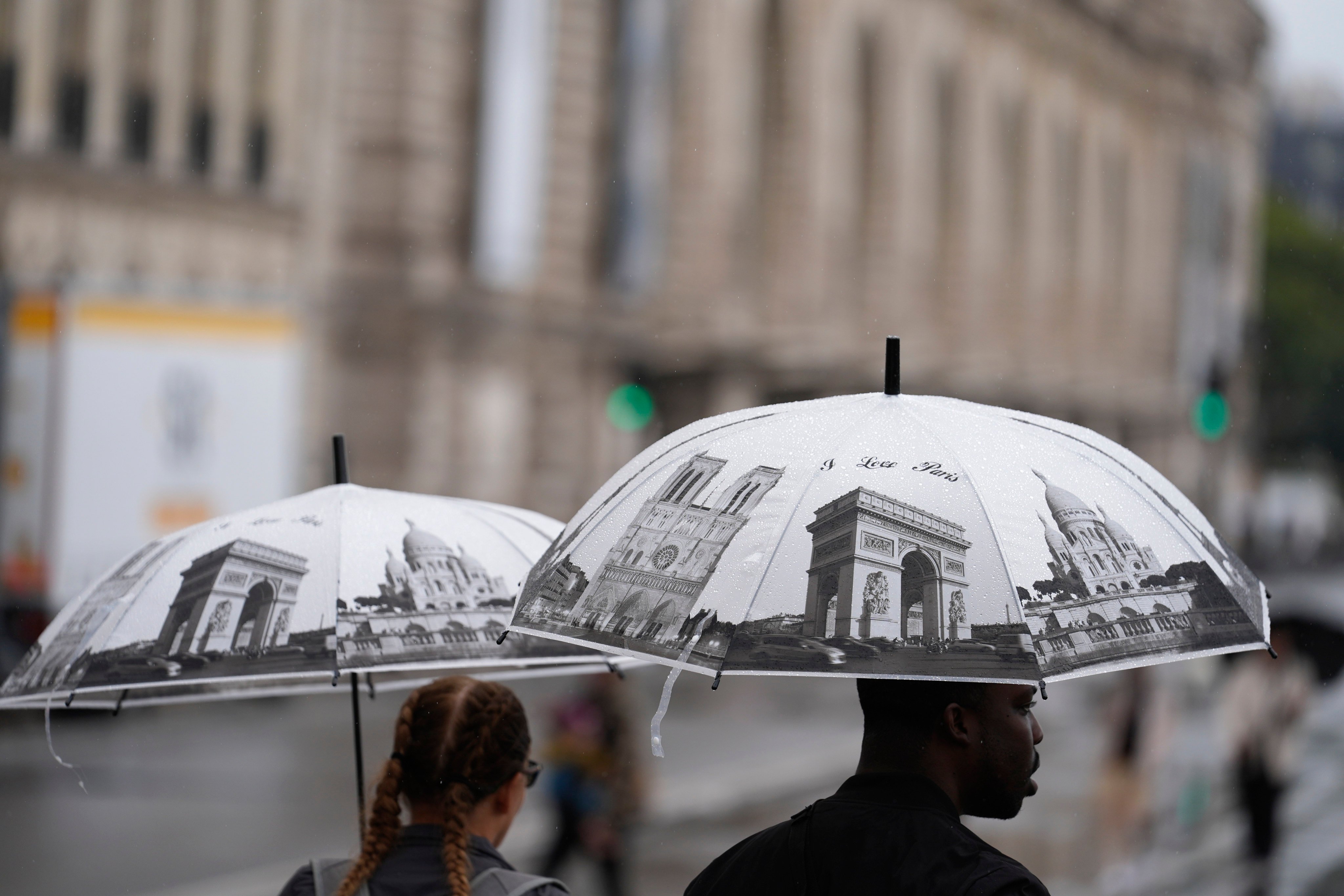 People with umbrellas depicting Paris landmarks walk down a road along the River Seine. Photo: AP