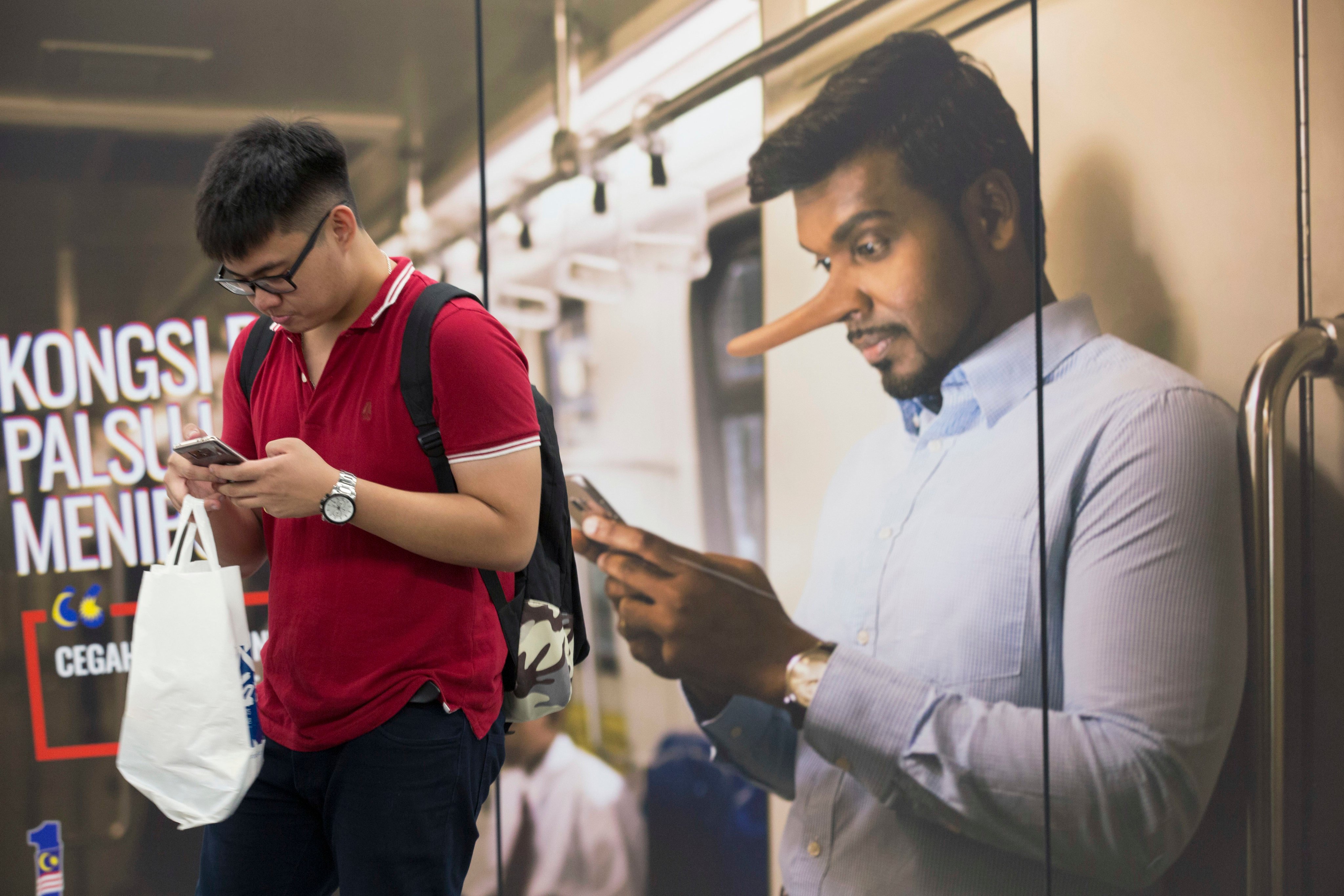 A commuter reads from his mobile phone next to an advertisement discouraging the dissemination of fake news at a train station in Kuala Lumpur, Malaysia. File photo: AP