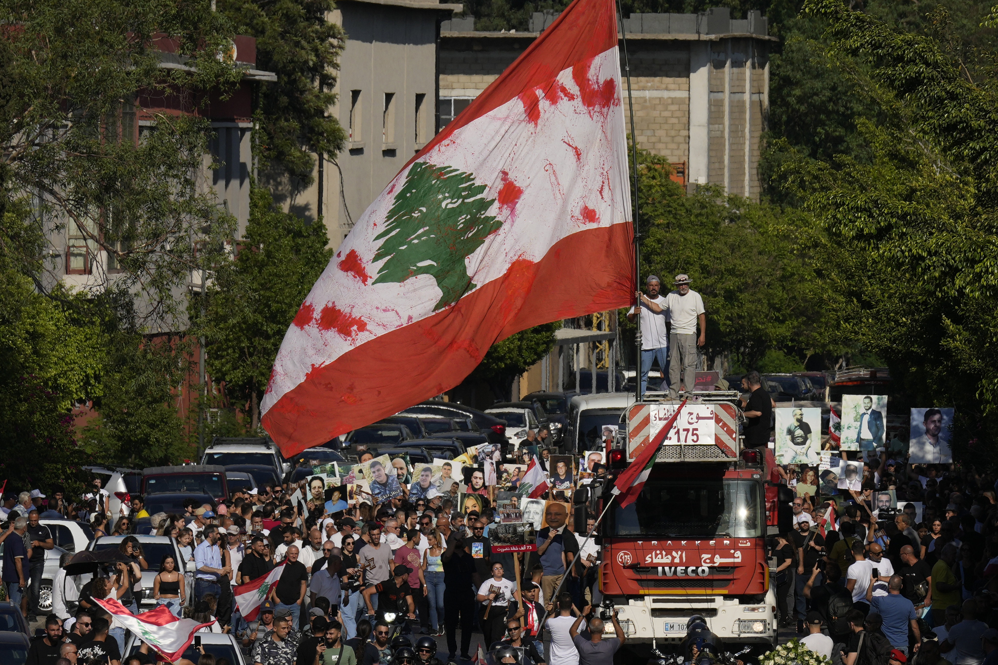 Relatives of victims who were killed in the 2020 Beirut port explosion stand on the ladder of a firetruck waving a giant Lebanese flag as others march with portraits of loved ones during the fourth anniversary of the explosion, in Beirut, Lebanon on Sunday. Photo: AP